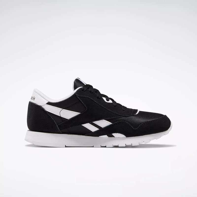 The Reebok Classic Nylon Shoes - Big Kids feature a black and white 80s-inspired minimalist design with side stripes, branding, and a white sole, shown in profile against a light background.