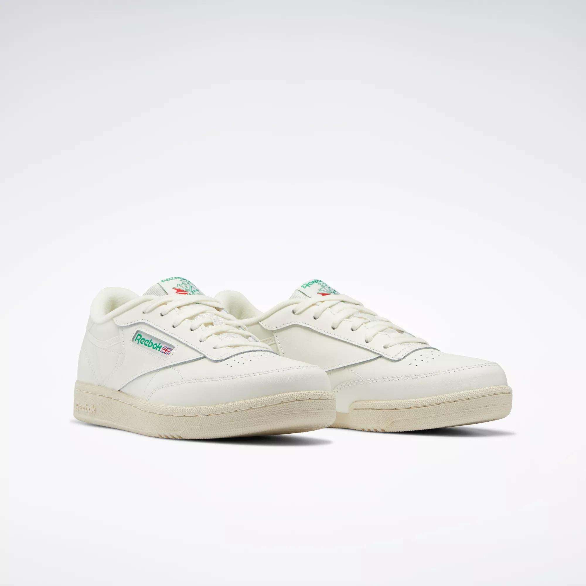 The Reebok Club C Shoes for big kids feature an off-white design with green and red logo details on the side and tongue, inspired by classic '80s style, set against a plain white background.