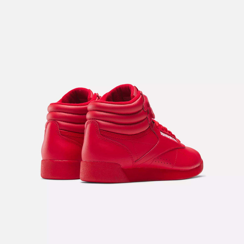 A pair of Women's Freestyle Hi Shoes by Reebok in bright red, featuring padded ankles and laces, are angled to display both sides and backs against a plain white background.