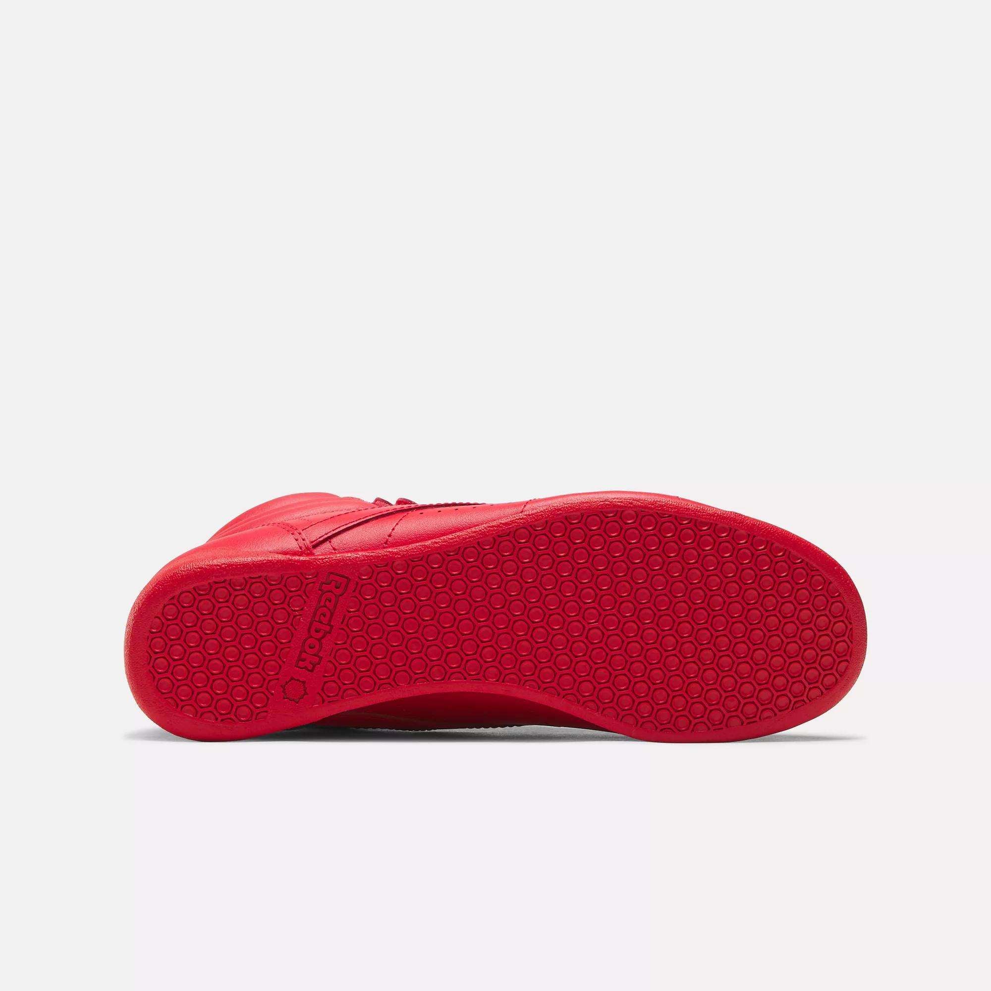 The Reebok Women's Freestyle Hi Shoes feature a bright red high-top design with a textured rubber sole, highlighted by a hexagonal pattern and the Reebok logo near the heel.