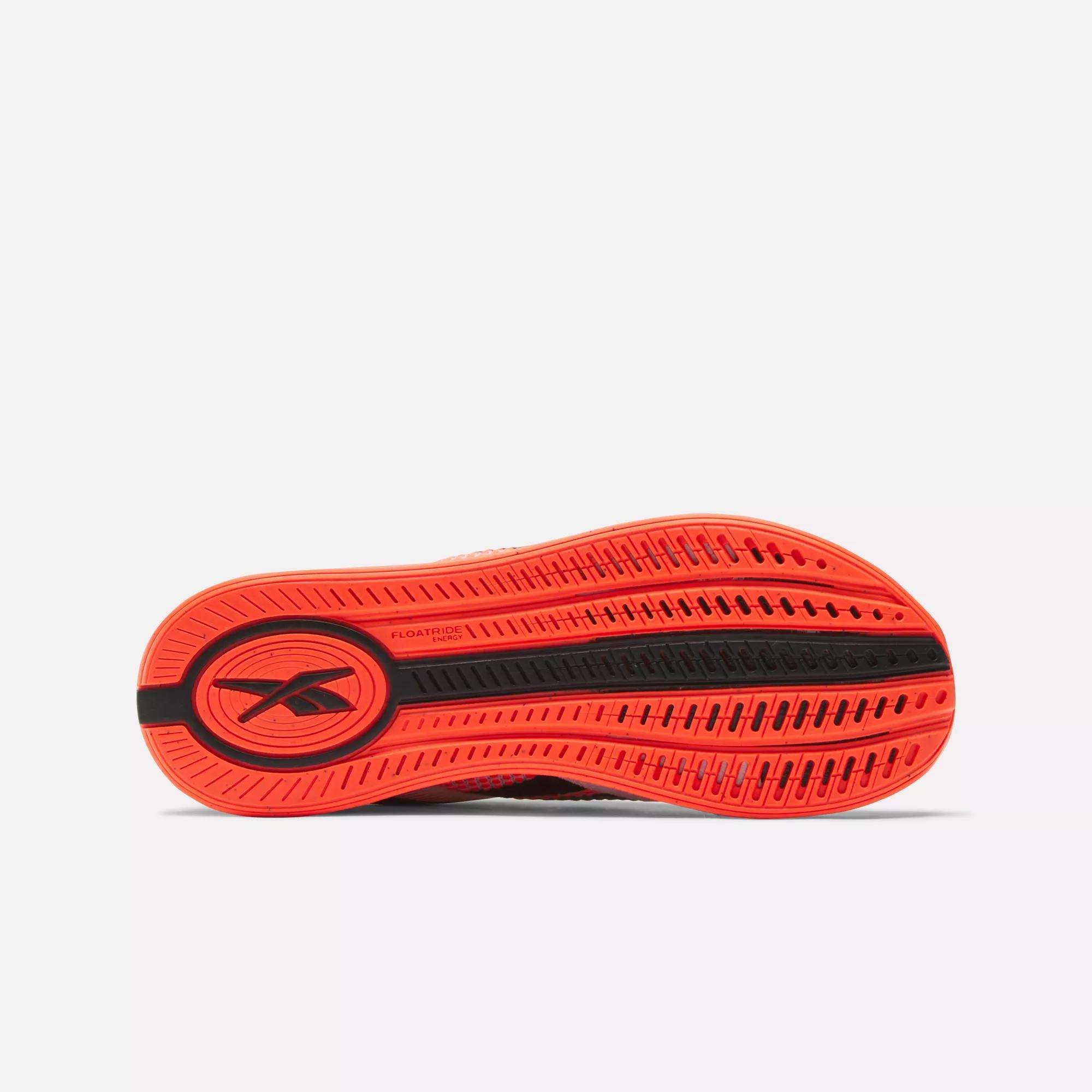 The image displays the bright orange sole of the Women's Nano X4 Training Shoes by Reebok, with a black Reebok logo and tread patterns for grip, shown horizontally against a plain white background.