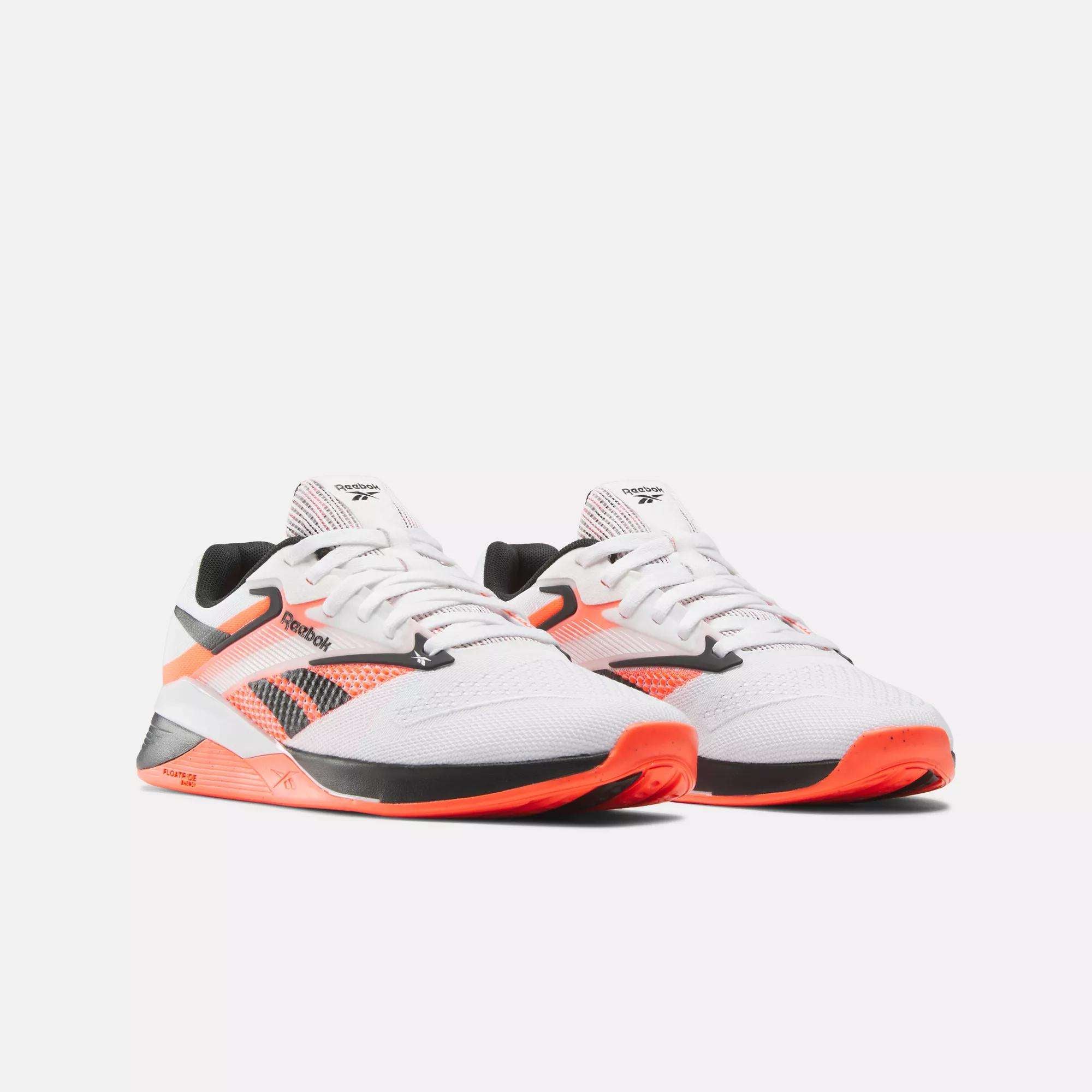 The Reebok Women's Nano X4 Training Shoes, featuring a white mesh upper with black and orange accents, black laces, and orange soles, are displayed on a plain white background, showcasing their lightweight training design.