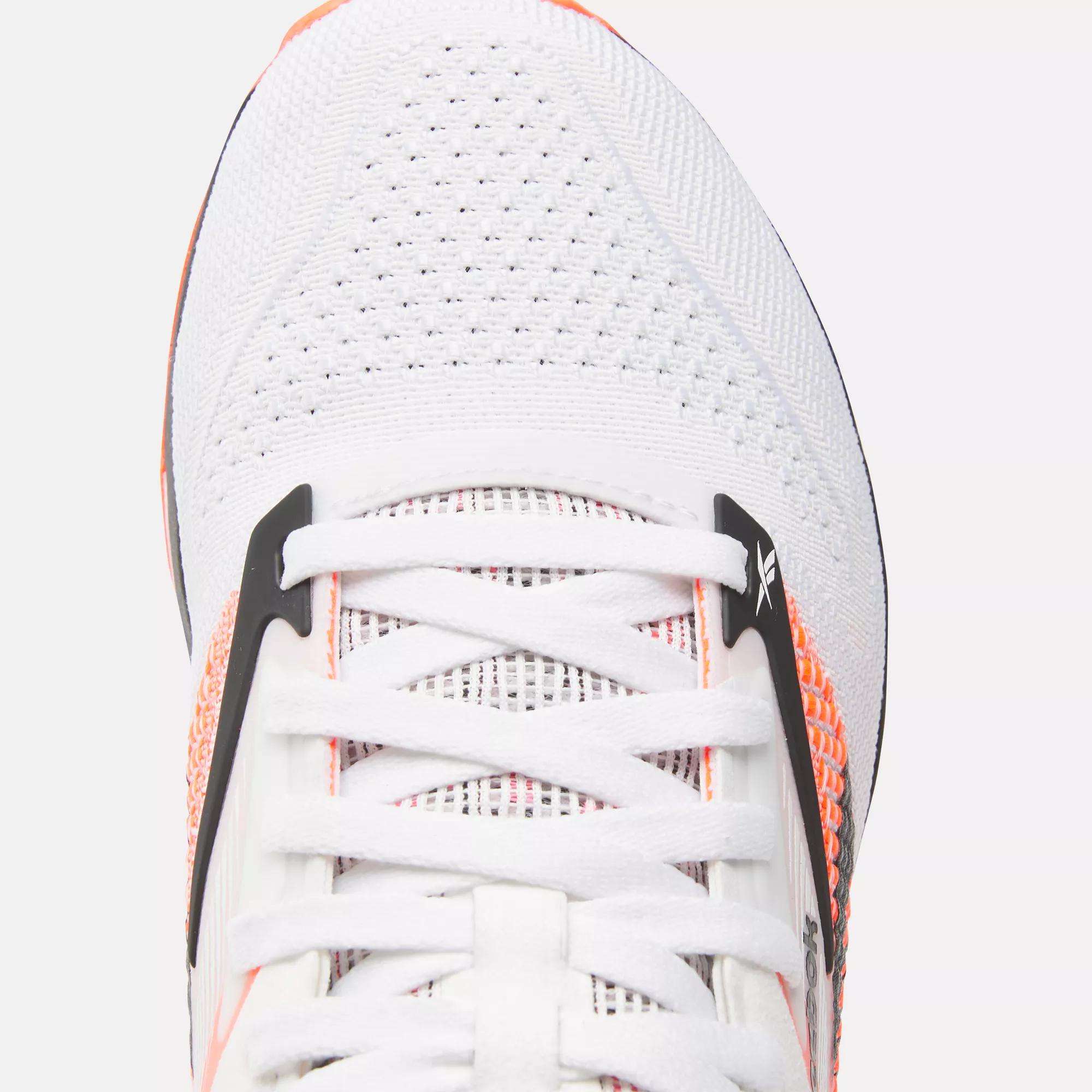 Close-up of Reebok Women's Nano X4 Training Shoes in white with orange accents and black details, featuring white laces and breathable mesh—ideal for those seeking lightweight training footwear.