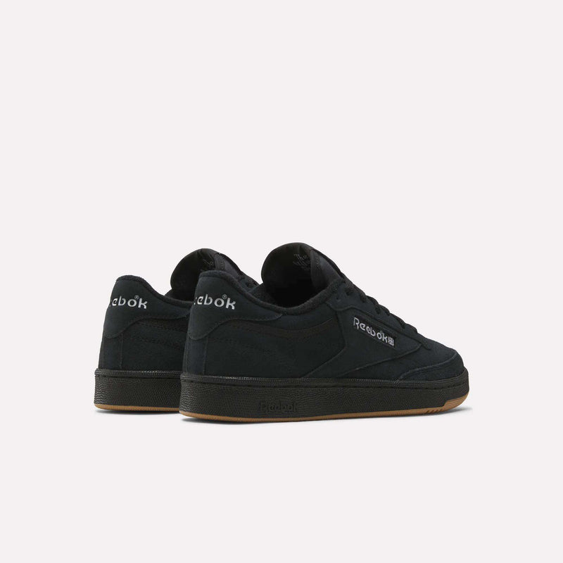 A pair of black Reebok Club C 85 Shoes with suede uppers and gum soles is displayed on a white background, one shoe facing forward and the other angled back, showcasing the court-inspired Reebok logos on the sides and heel.
