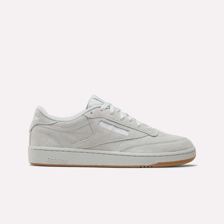 A side view of the Reebok Club C 85 Shoes in light grey suede with white laces, a slightly off-white sole, and a light brown gum bottom. The Reebok logo is displayed on the side and heel.