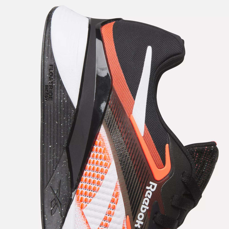 Close-up of the Reebok Nano X4 Training Shoes in black with white, orange, and red accents, featuring a breathable mesh upper, lightweight thick textured sole, and visible branding on the side and heel.