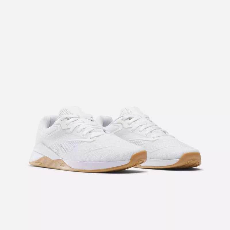 A pair of Reebok Women's Nano X4 Training Shoes with white uppers, matching laces, and light brown rubber soles are displayed side by side on a plain white background, highlighting their lightweight and breathable design.
