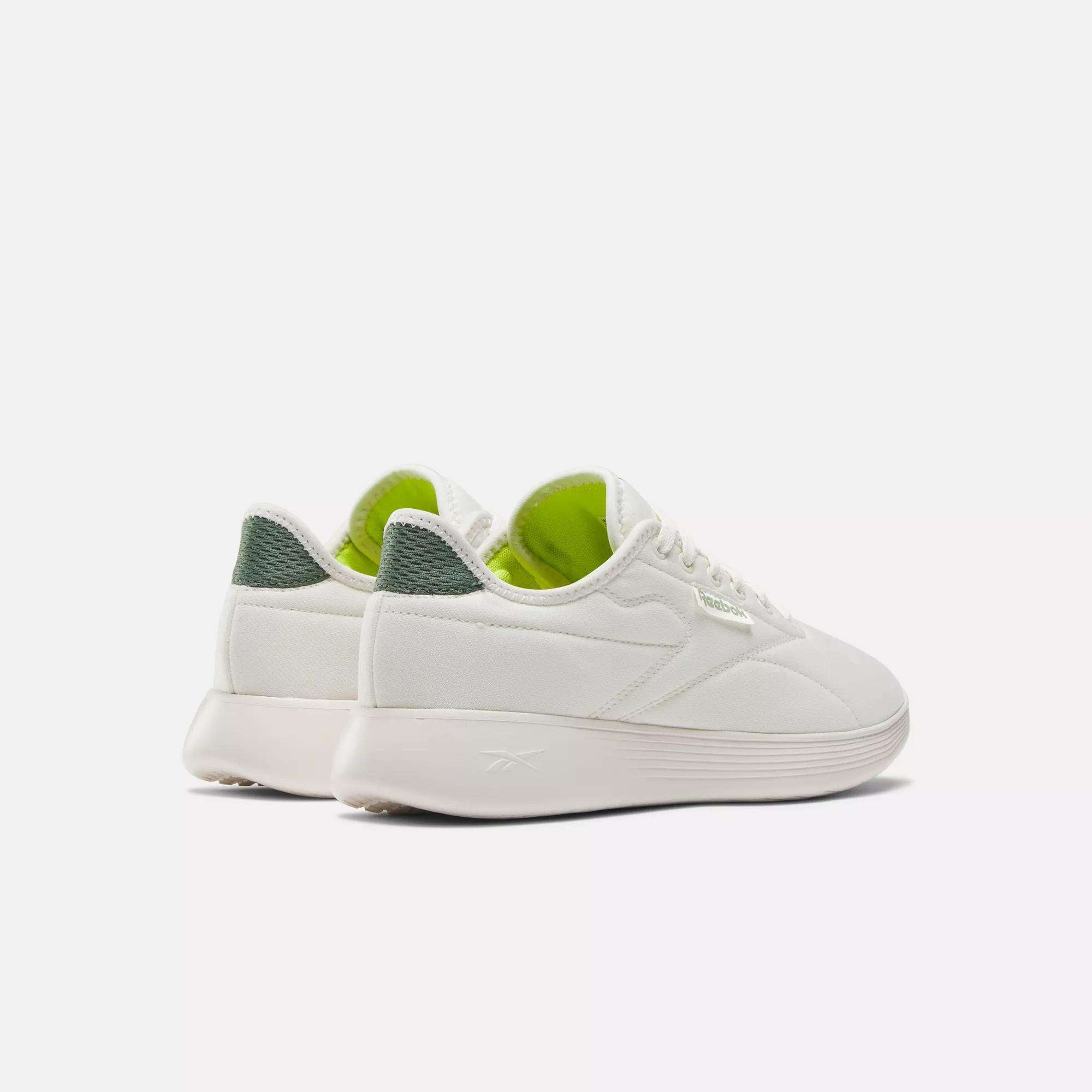 A pair of Reebok Active Lite Shoes in white, featuring light green interiors and dark green textured detailing on the heel, displayed from an angled rear view against a plain white background.