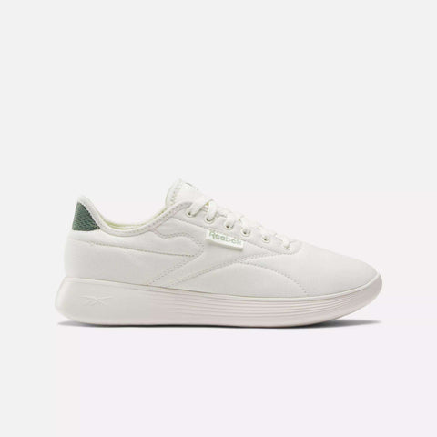 The Reebok Active Lite Shoes are white minimalist sneakers with a low profile, white laces, a textured sole, green heel accent, and a breathable upper for all-day comfort. Shown on a plain white background.