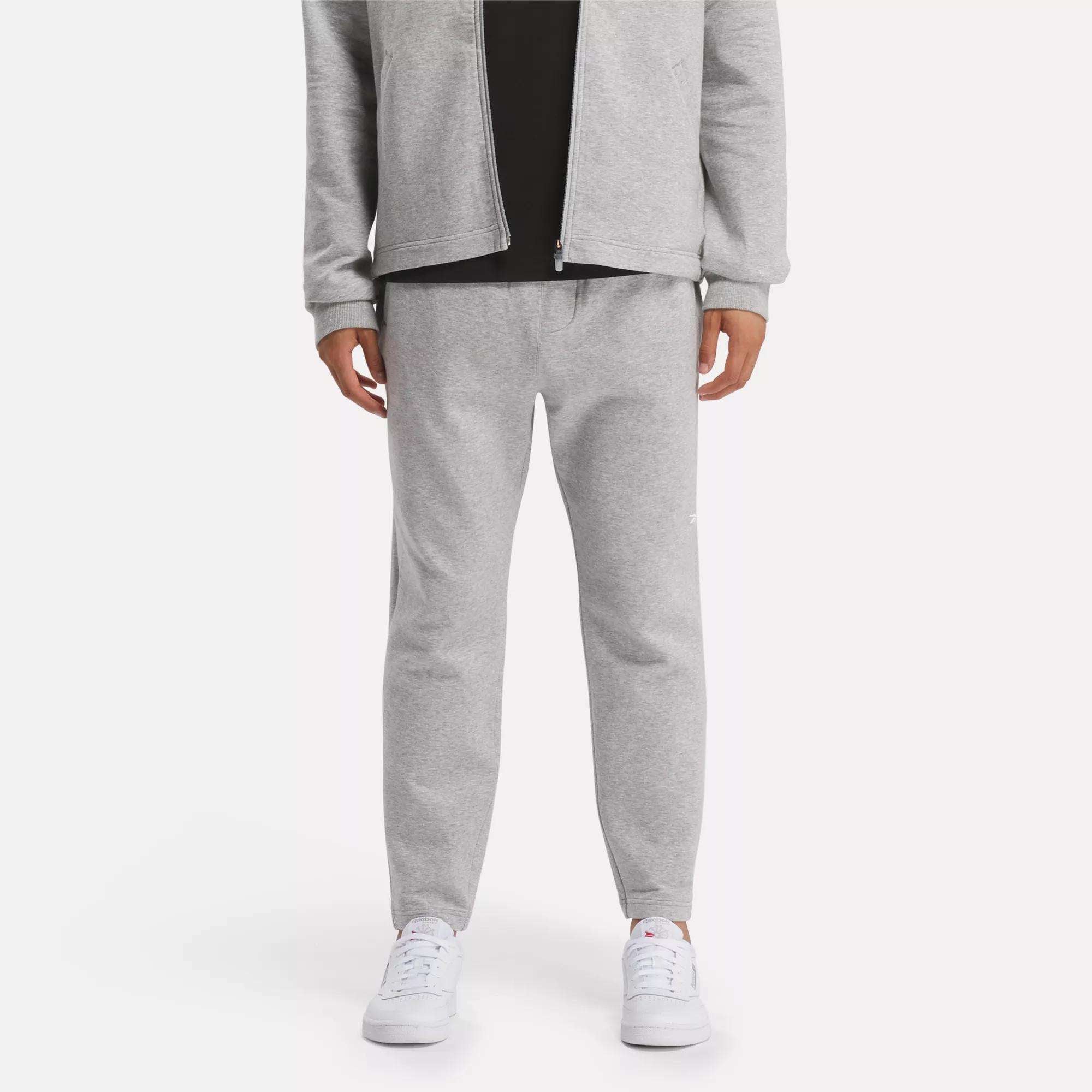 A person in a light gray zip-up jacket and Reebok Men's Active Collective DreamBlend Pants with white sneakers stands against a plain light background; their face is not visible.