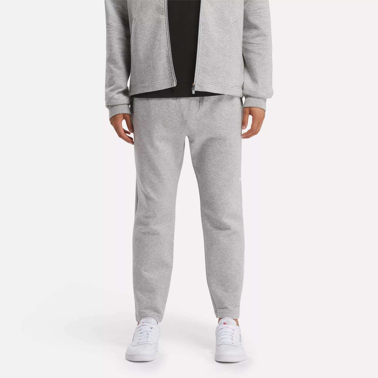 A person in a light gray zip-up jacket and Reebok Men's Active Collective DreamBlend Pants with white sneakers stands against a plain light background; their face is not visible.
