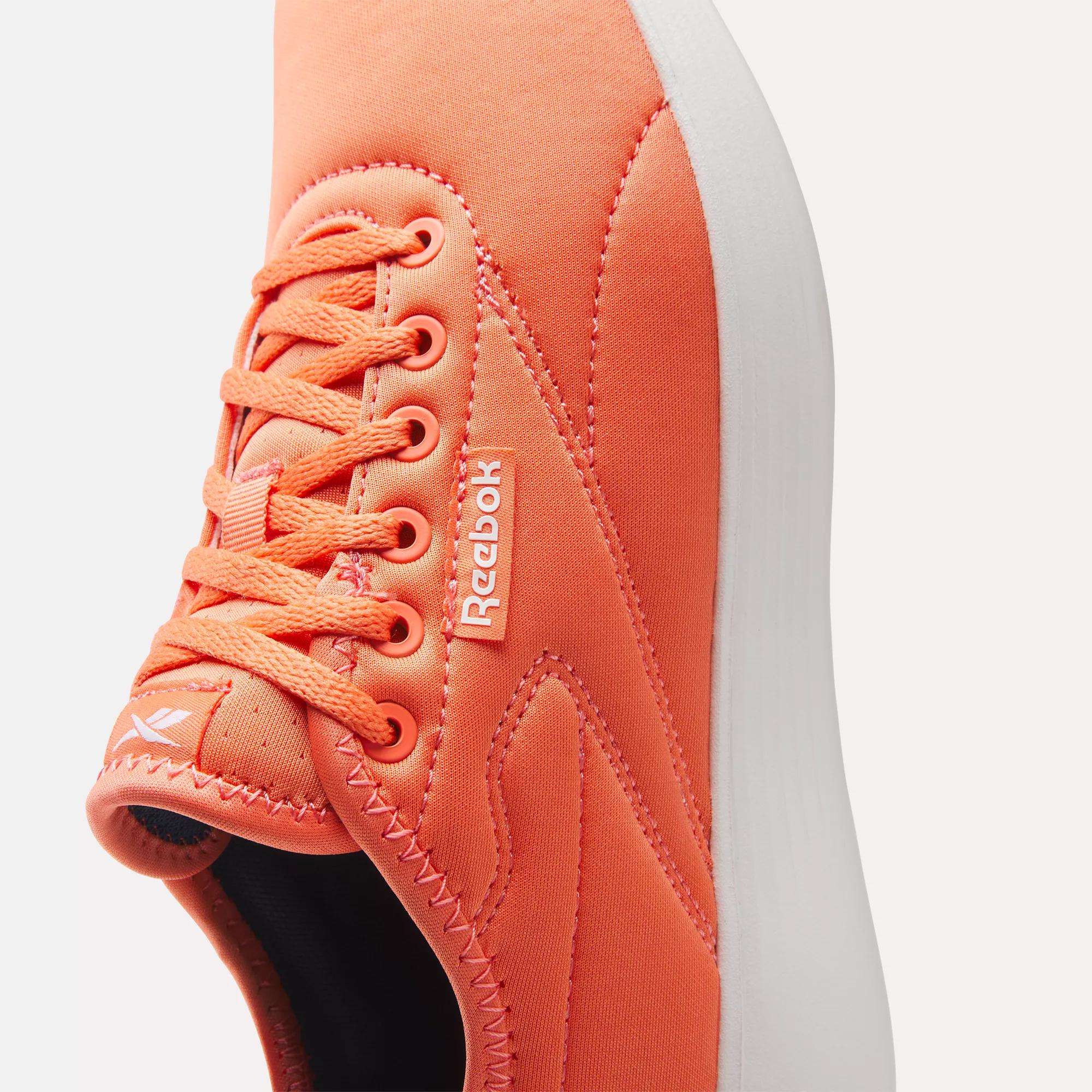Close-up of the Women's Active Lite Shoes by Reebok—orange sneaker with detailed stitching, laces, a Reebok logo tag, DMX technology in the sole, and part of the white sole shown against a light background.