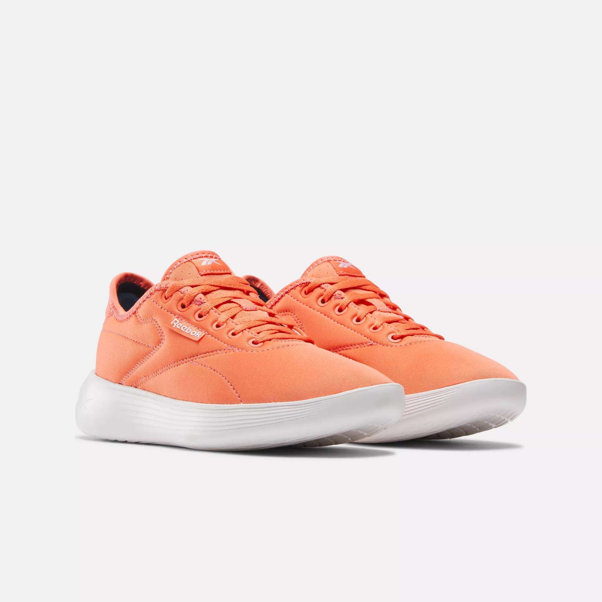 A pair of Women's Active Lite Shoes by Reebok in bright orange, featuring a minimalist sneaker design with white soles, displayed from an angled side view on a plain white background.