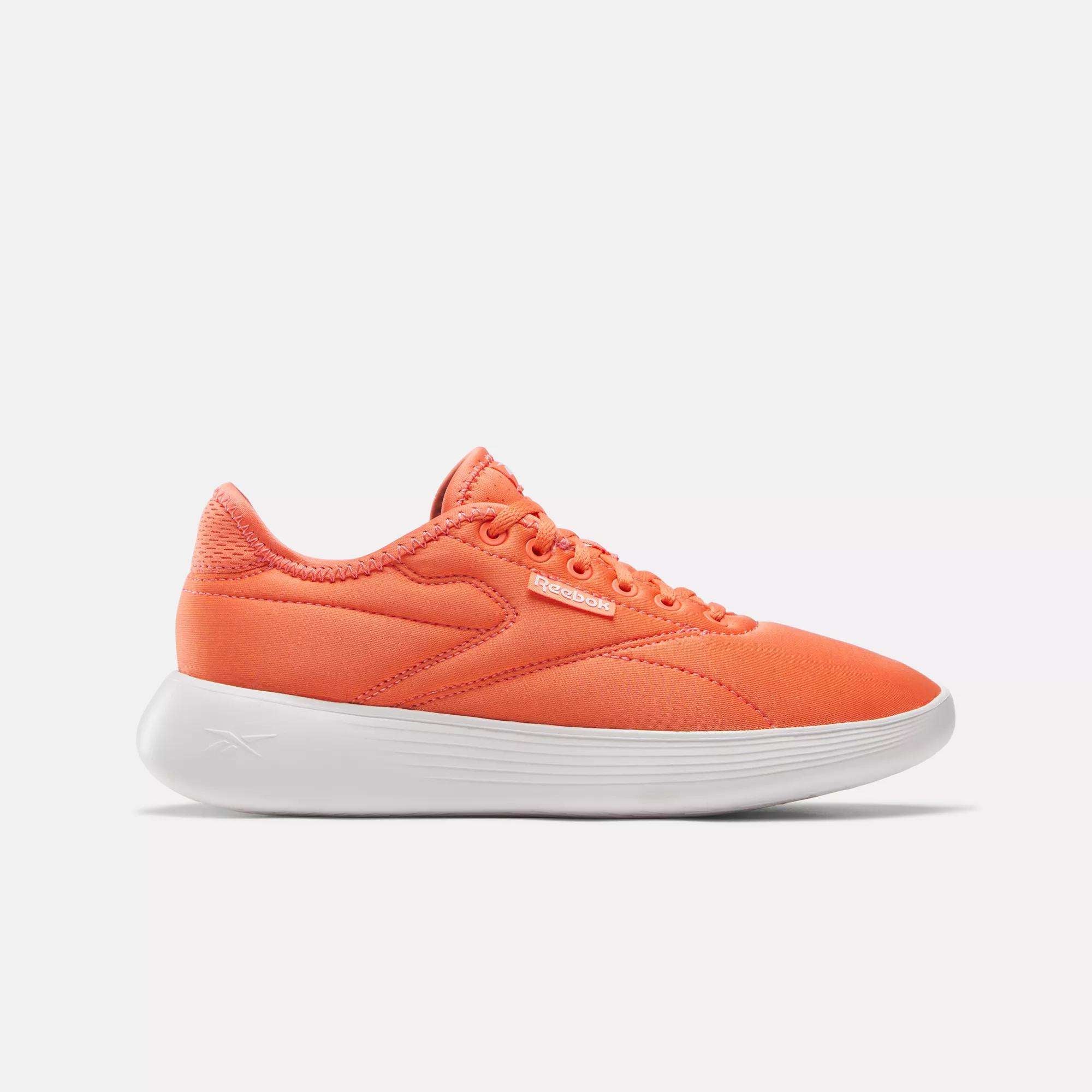 The Reebok Women's Active Lite Shoes feature a bright orange design, matching laces, DMX technology, and a thick white sole. Shown from the side on a plain white background.