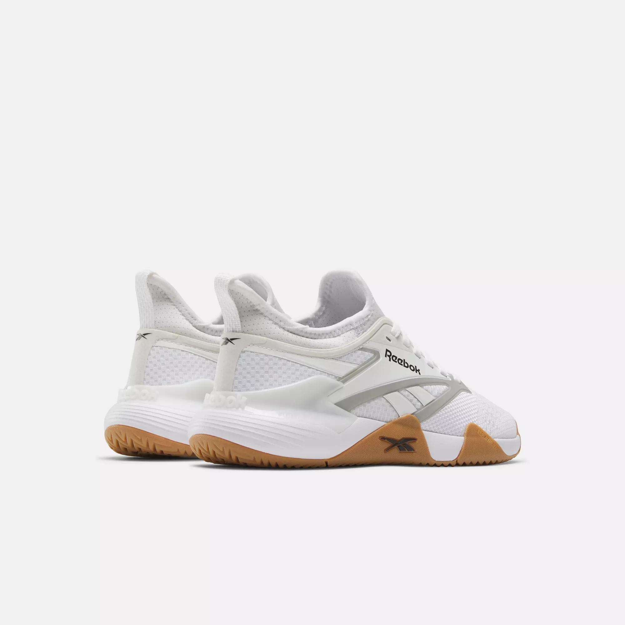 A pair of Reebok Women's Nano Court Training Shoes in white, featuring mesh uppers, gray branding, and Griptonite gum rubber soles, are shown against a plain white background with a back and side view.