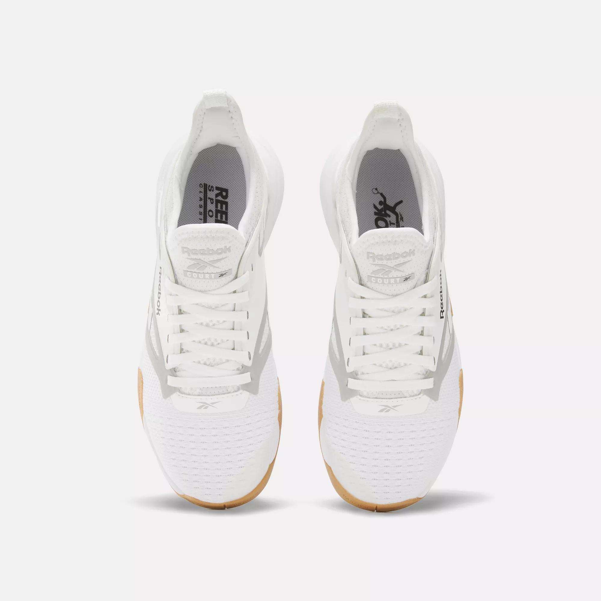 The Reebok Women's Nano Court Training Shoes are shown top-down on a white background, featuring white uppers, gum soles, and white laces with multidirectional traction designed for court sports.