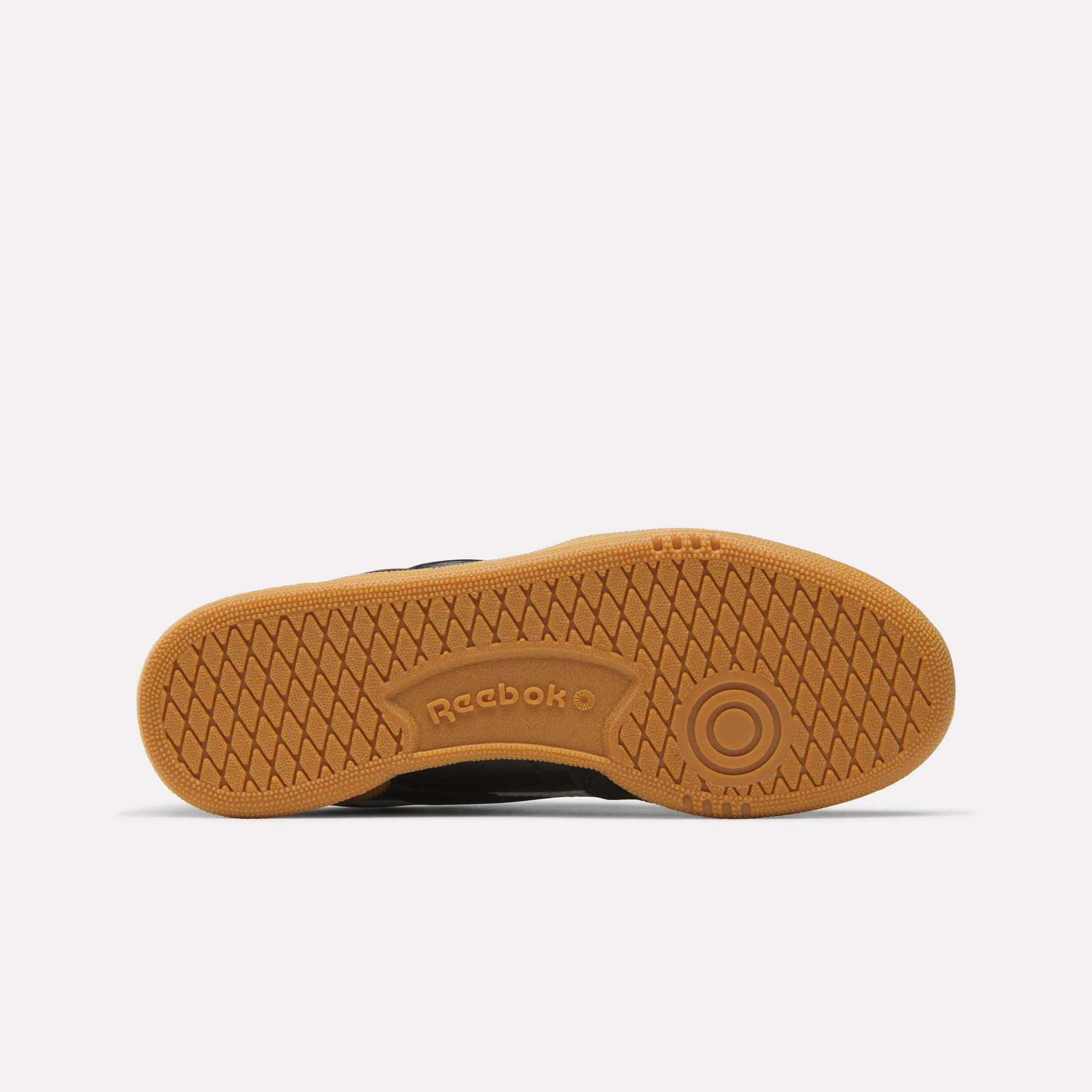 The image shows the gum-colored sole of Reebok Club C Revenge Vintage Shoes, featuring a textured criss-cross tread, the Reebok logo by the arch, and a circular design near the toe—details often seen on retro styles.