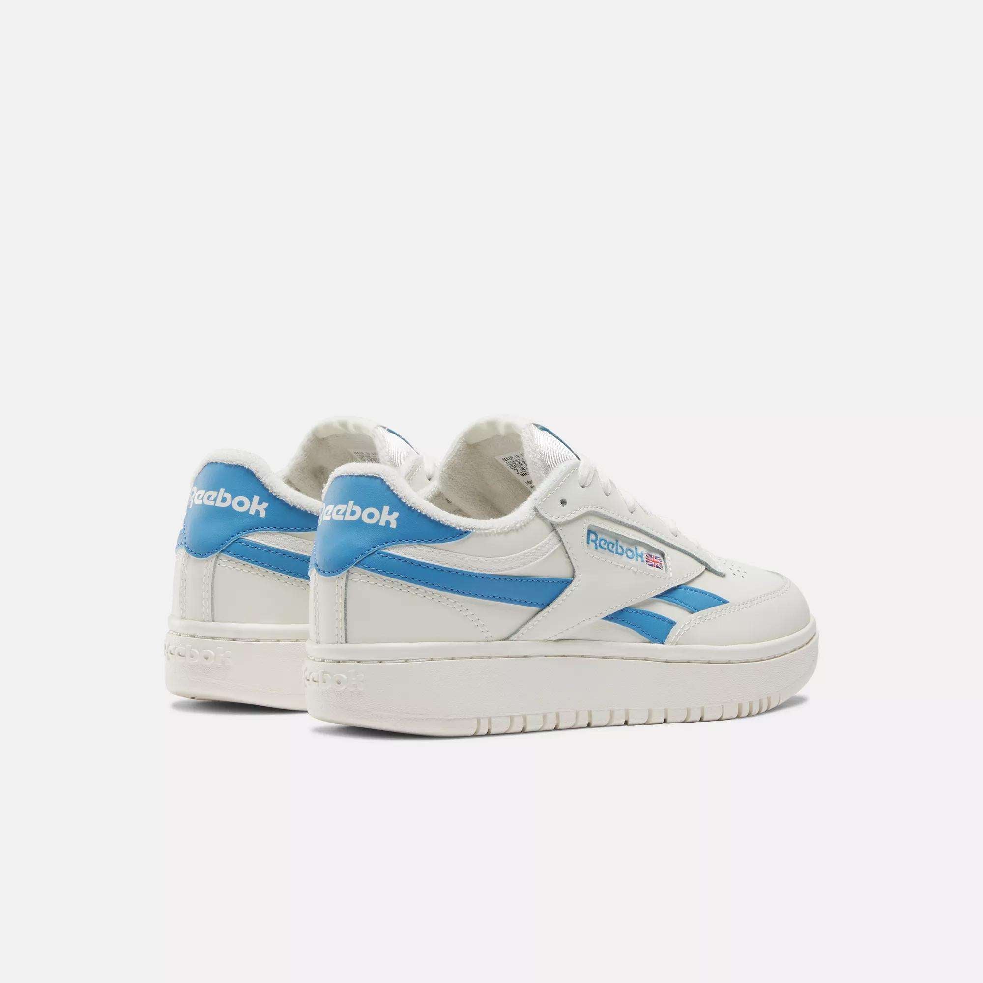 The Women's Club C Double Revenge Shoes by Reebok are white court-inspired sneakers with blue accents and logos, featuring a leather upper. Displayed on a plain light background, their angled position shows both side and back details.
