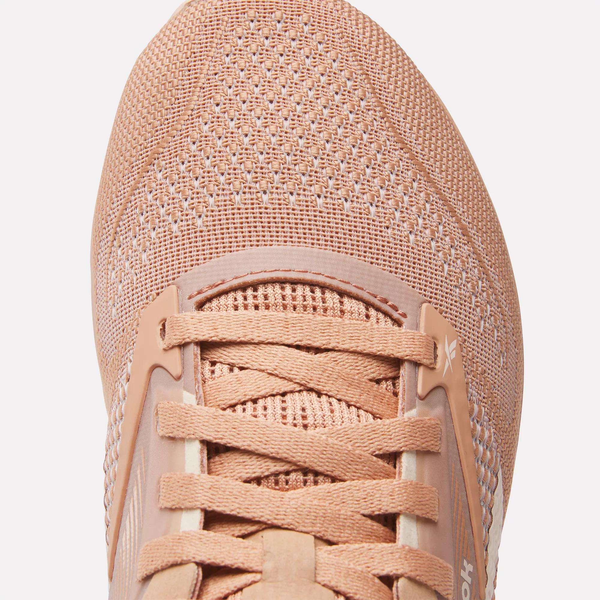 Close-up of Reebok Women's Nano X4 Training Shoes in peach, highlighting their lightweight mesh upper, laces, part of the tongue with visible stitching, and breathable texture details.