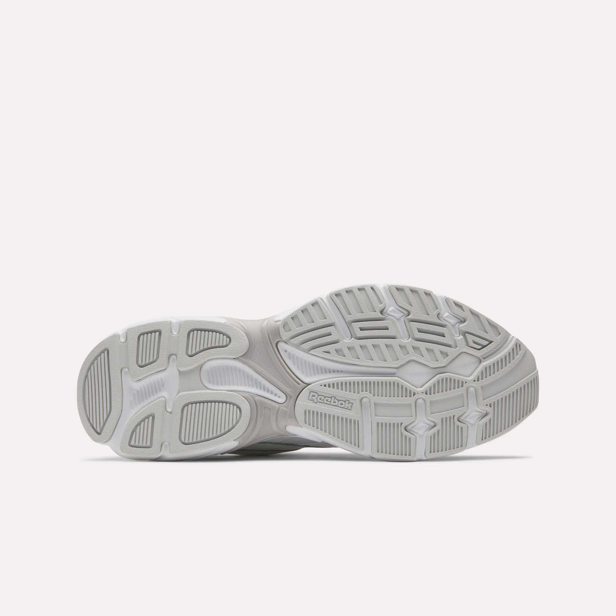 The image displays the gray, textured rubber sole of Reebok Road Prime Shoes against a white background, featuring varied tread patterns and the Reebok logo near the center, reflecting classic Y2K running style.