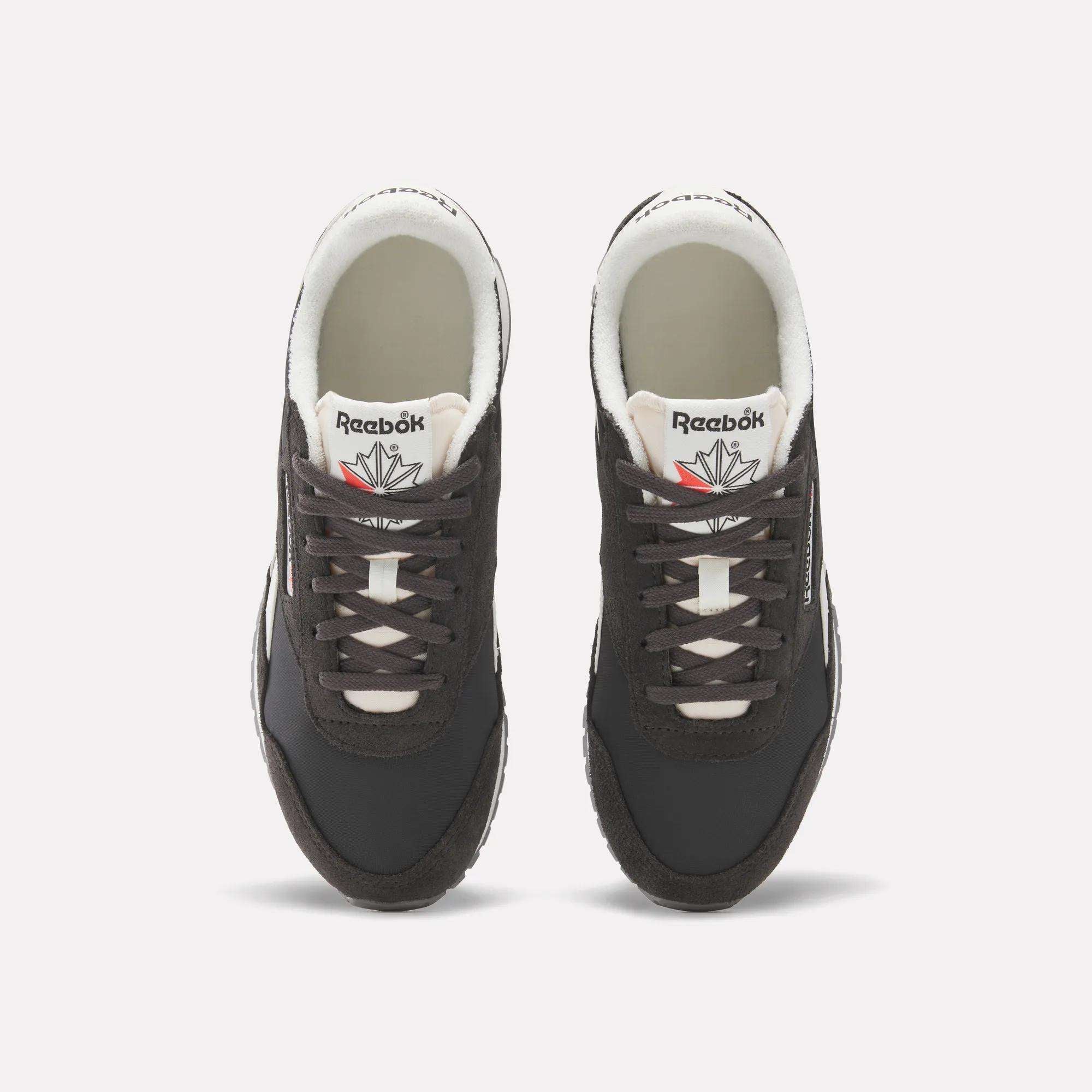 A pair of Women's Classic AZ Shoes by Reebok in black, featuring white soles and laces, are shown from above on a plain white background. The Reebok logo and a red and gray star appear on the tongues.