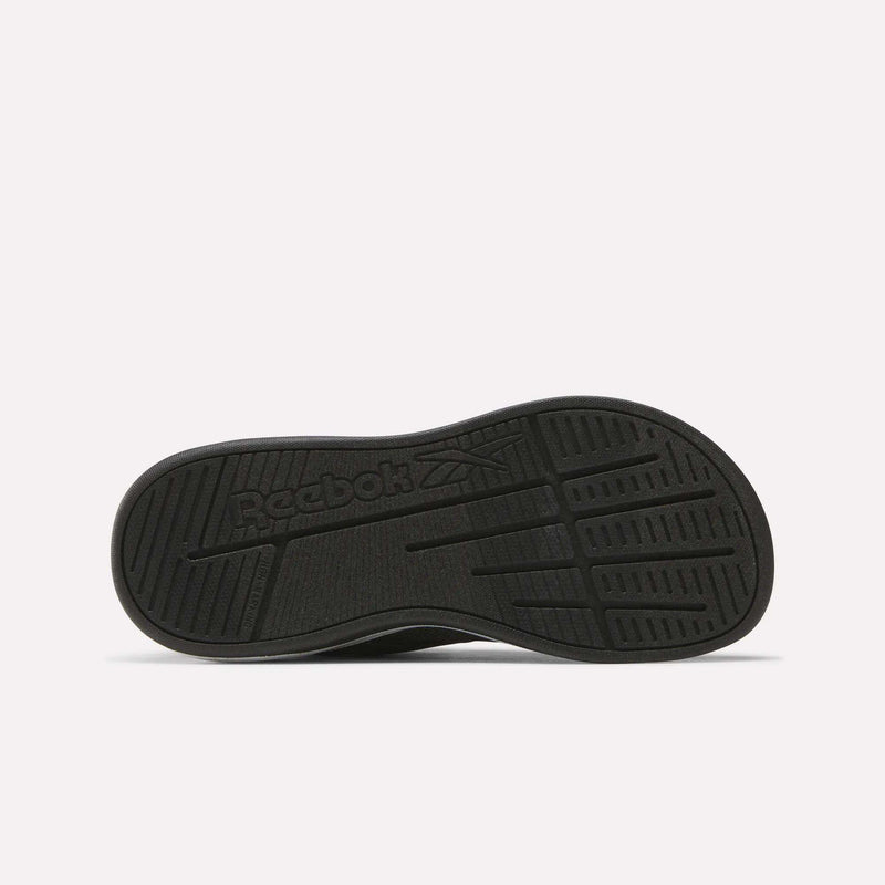 The image shows the black rubber outsole of the Reebok Nano Play Stretch Lace And Top Strap Shoes for little kids, with textured grip patterns and an embossed Reebok logo featuring the brand's vector symbol in the center.