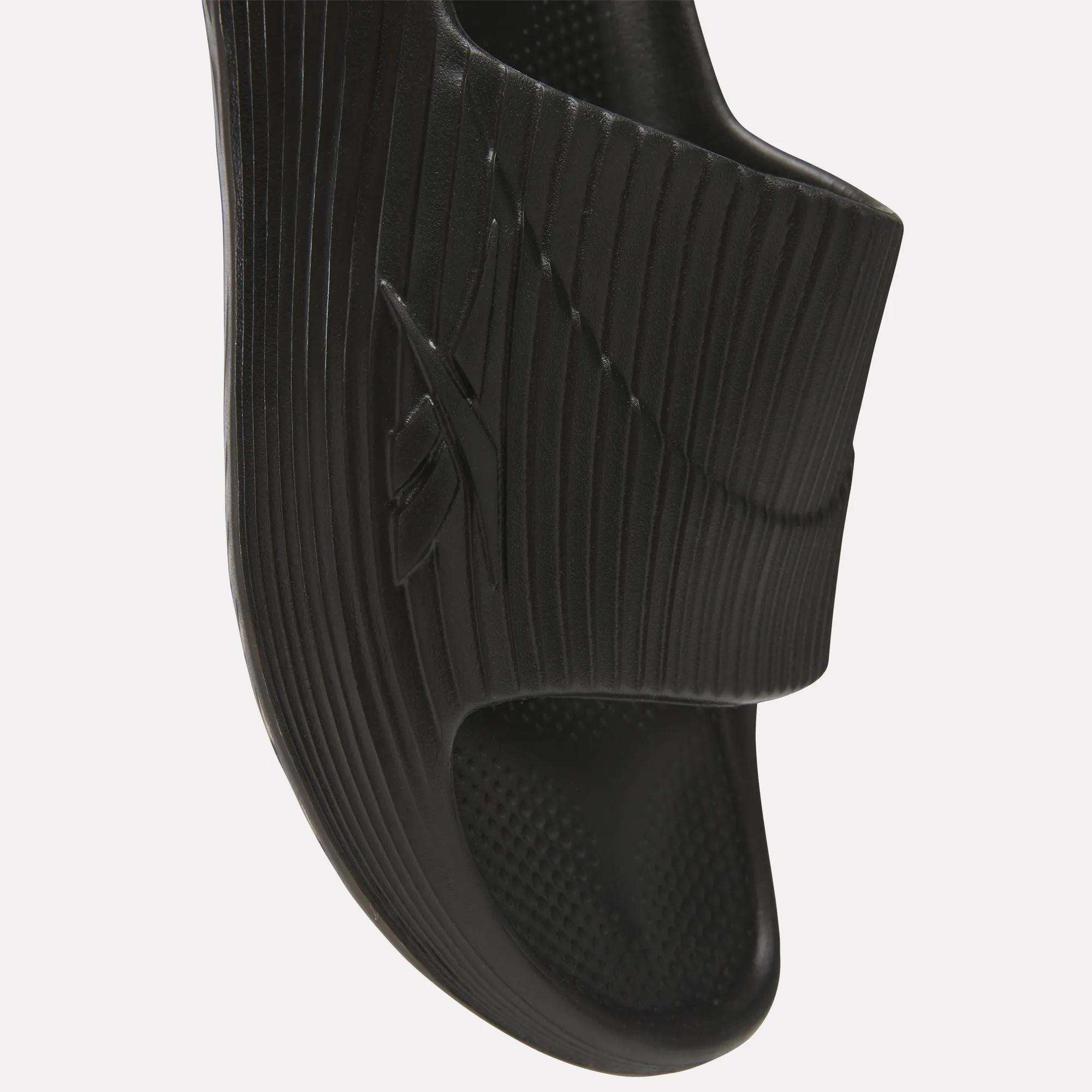 Close-up of a black Reebok DMX Recovery Walking Slide featuring a textured strap with the embossed Reebok logo, ridged sole, and super-soft foam for all-day comfort.