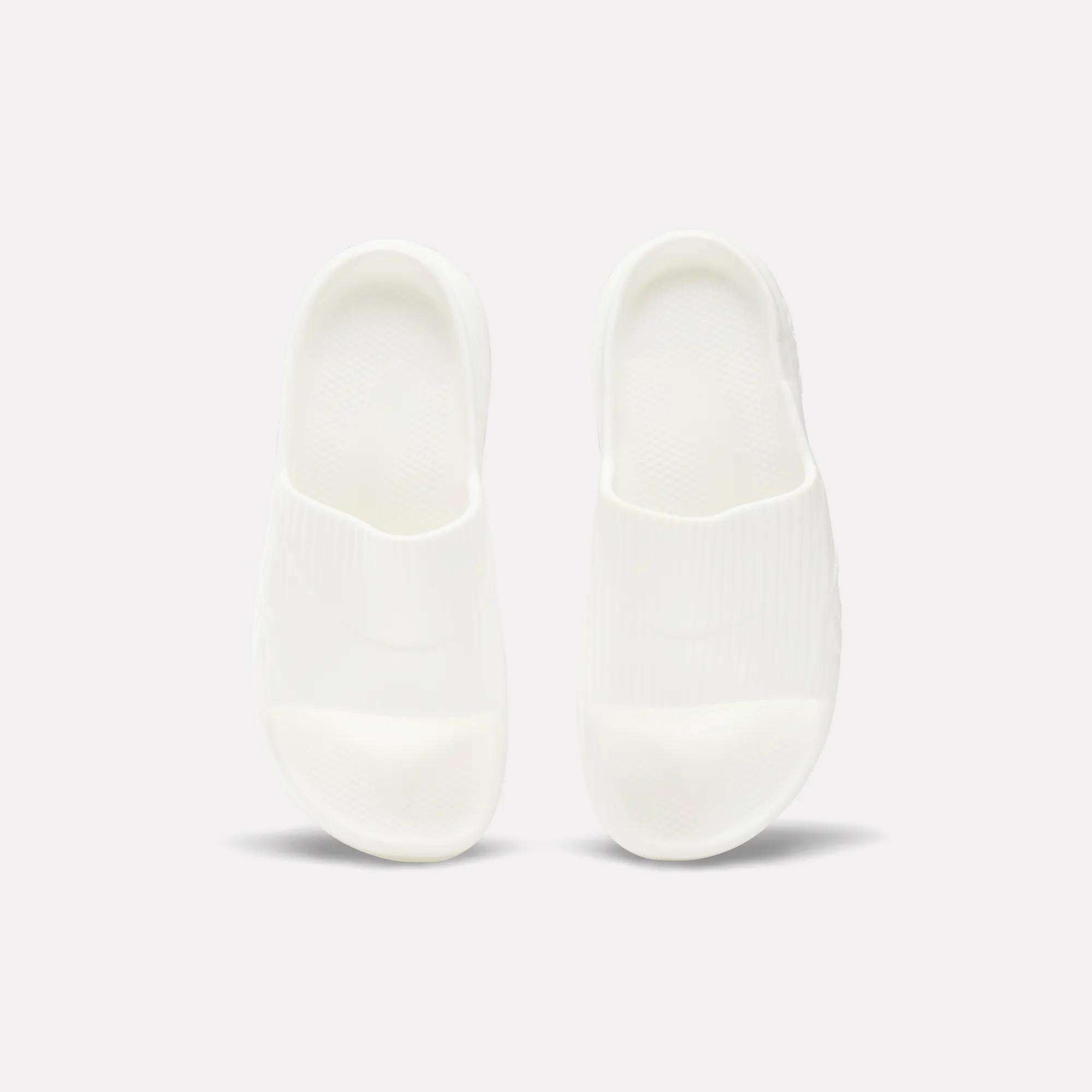 A pair of Reebok DMX Recovery Walking Slides in plain white are placed side by side on a light background, viewed from above.