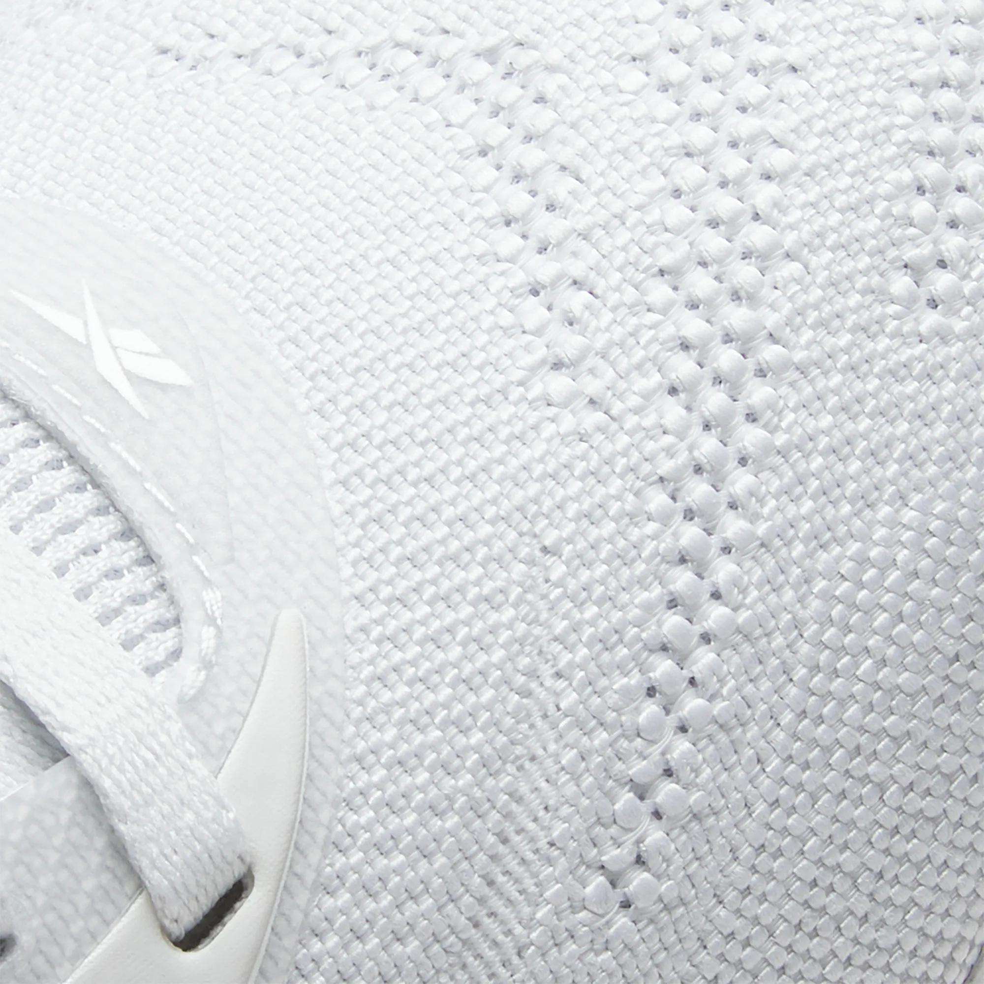 Close-up of Reebok Women's Nano X5 Training Shoes in white, featuring a textured knit-like fabric, partial white shoelace, and subtle side logo, emphasizing their comfortable design for women.