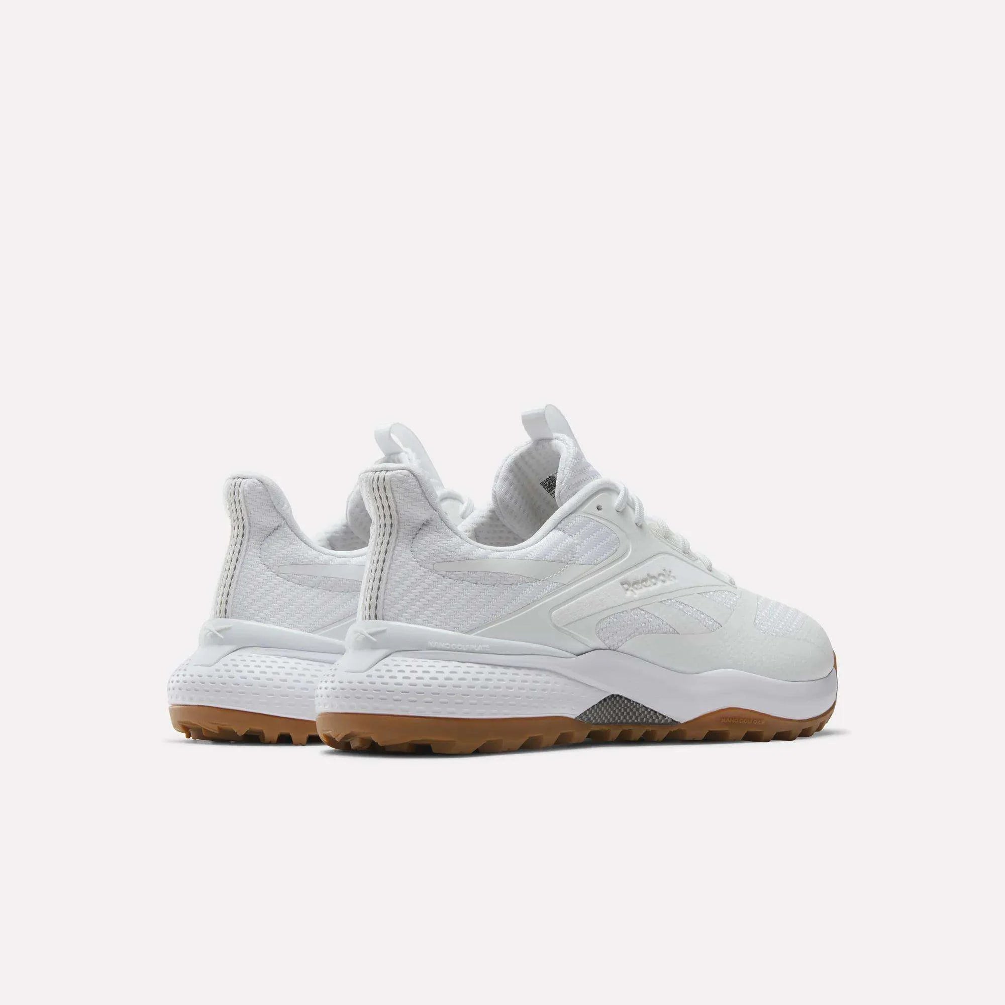 A pair of white Reebok athletic sneakers with textured detailing, white laces, and light brown rubber soles, shown from a rear-side angle on a plain white background.