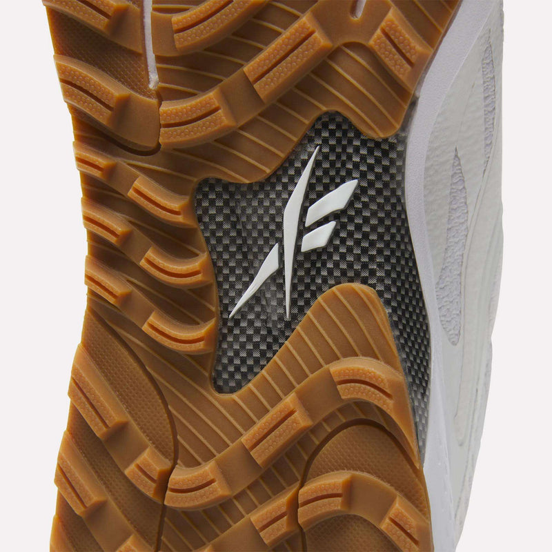 Close-up of Reebok Nano Golf Shoes shows a textured gum rubber sole, black carbon fiber-like midfoot, white logo, white leather overlays, breathable FlexWeave mesh, and golf-inspired advanced performance design on the side.