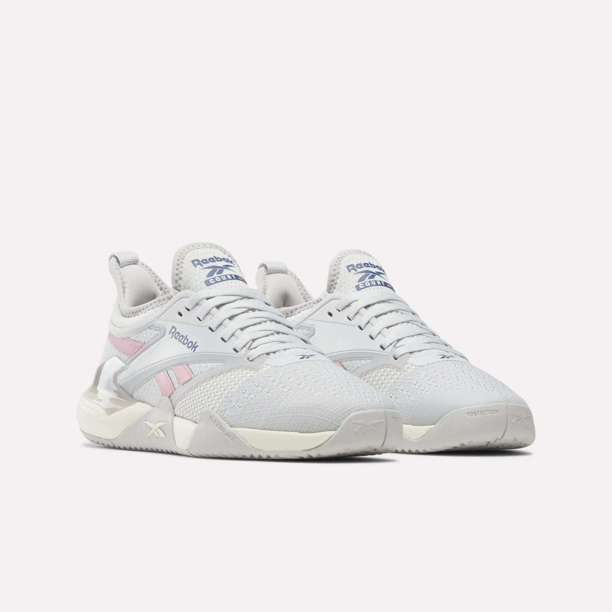A pair of Reebok Women's Nano Court Training Shoes with mesh uppers, light pink and blue accents, off-white soles, and a Griptonite rubber outsole are shown side by side on a plain white background.