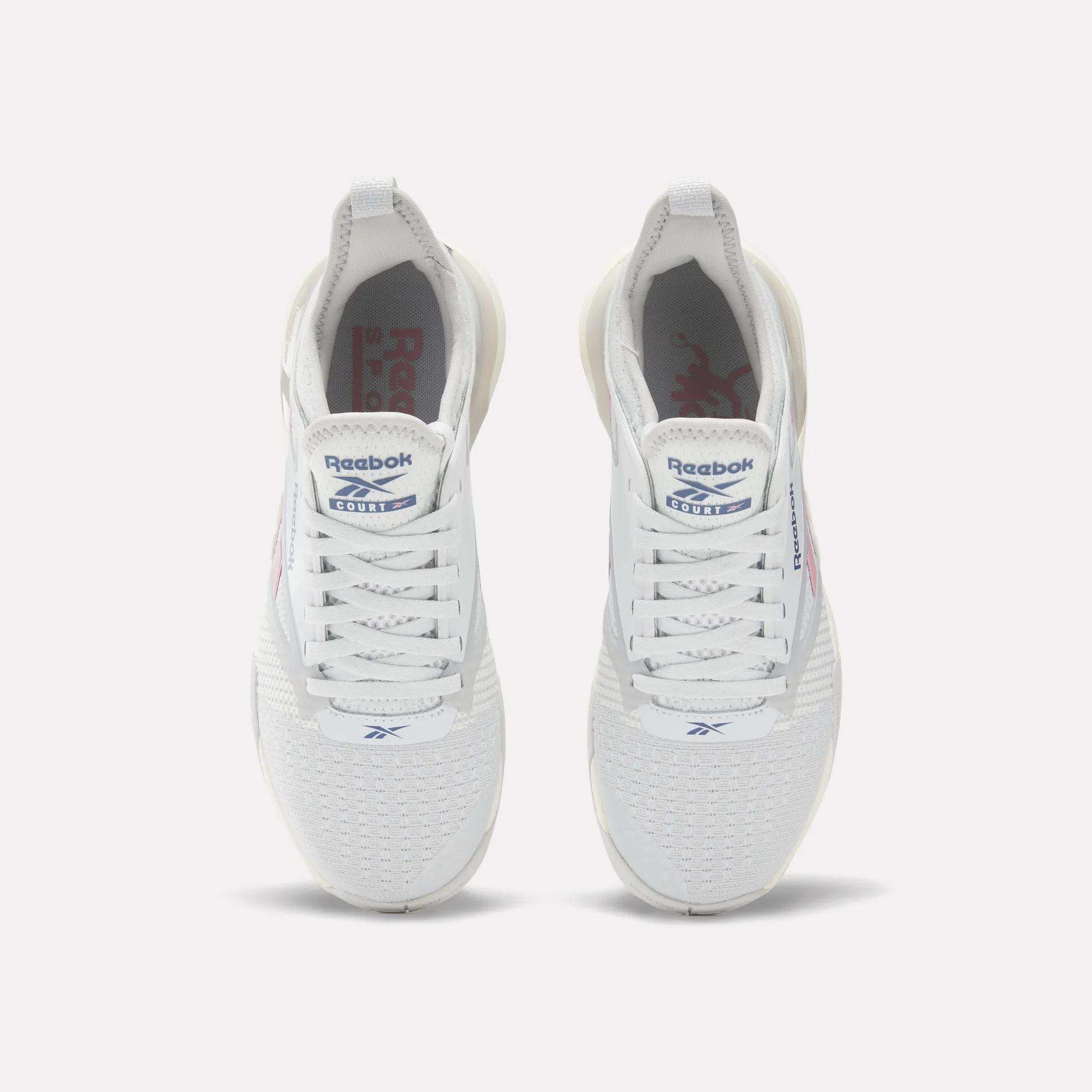 A pair of Reebok Women's Nano Court Training Shoes shown from above, with mesh uppers, white laces, blue Reebok logos on the tongues, subtle red branding on sides and insoles, and a durable Griptonite rubber outsole for court sports.