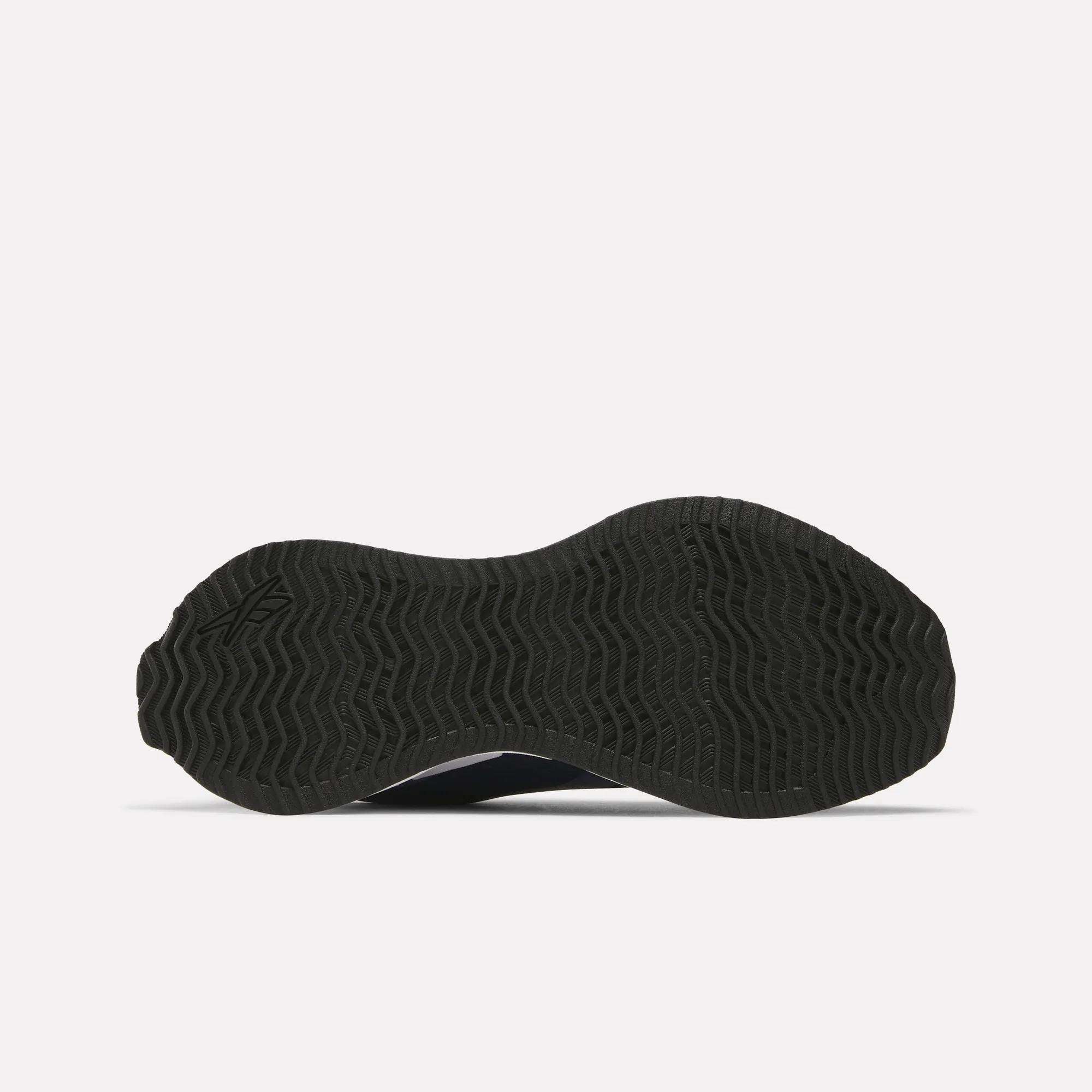The bottom of the Reebok Women's Zig Dynamica STR Shoes is shown, featuring a black sole with a wavy tread pattern against a plain white background.