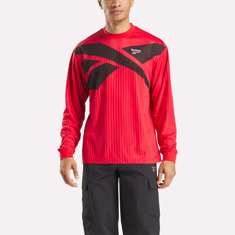 A man sports the Crosscheck Long Sleeve Jersey in red, featuring a prominent black logo on the chest, paired with black cargo pants for a sporty style against a plain white background.