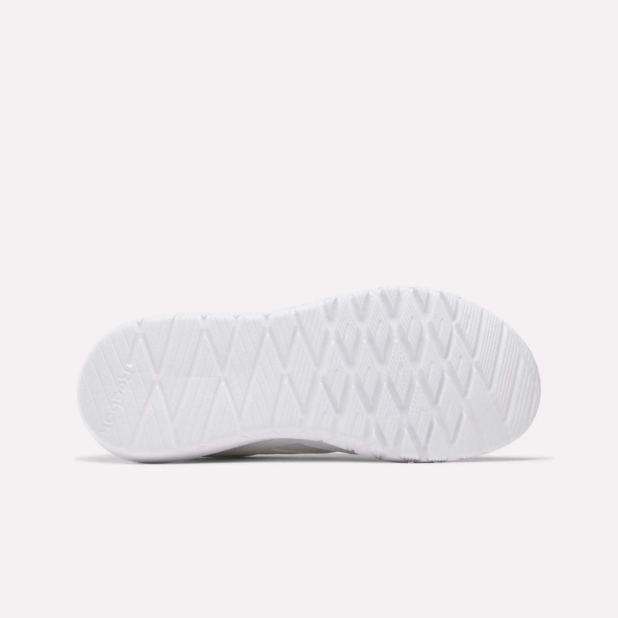 The image shows the bottom view of a white Reebok Women's Flexagon Energy 4 Training Shoe sole with a textured, diamond-patterned tread and responsive cushioning, set against a plain light background.