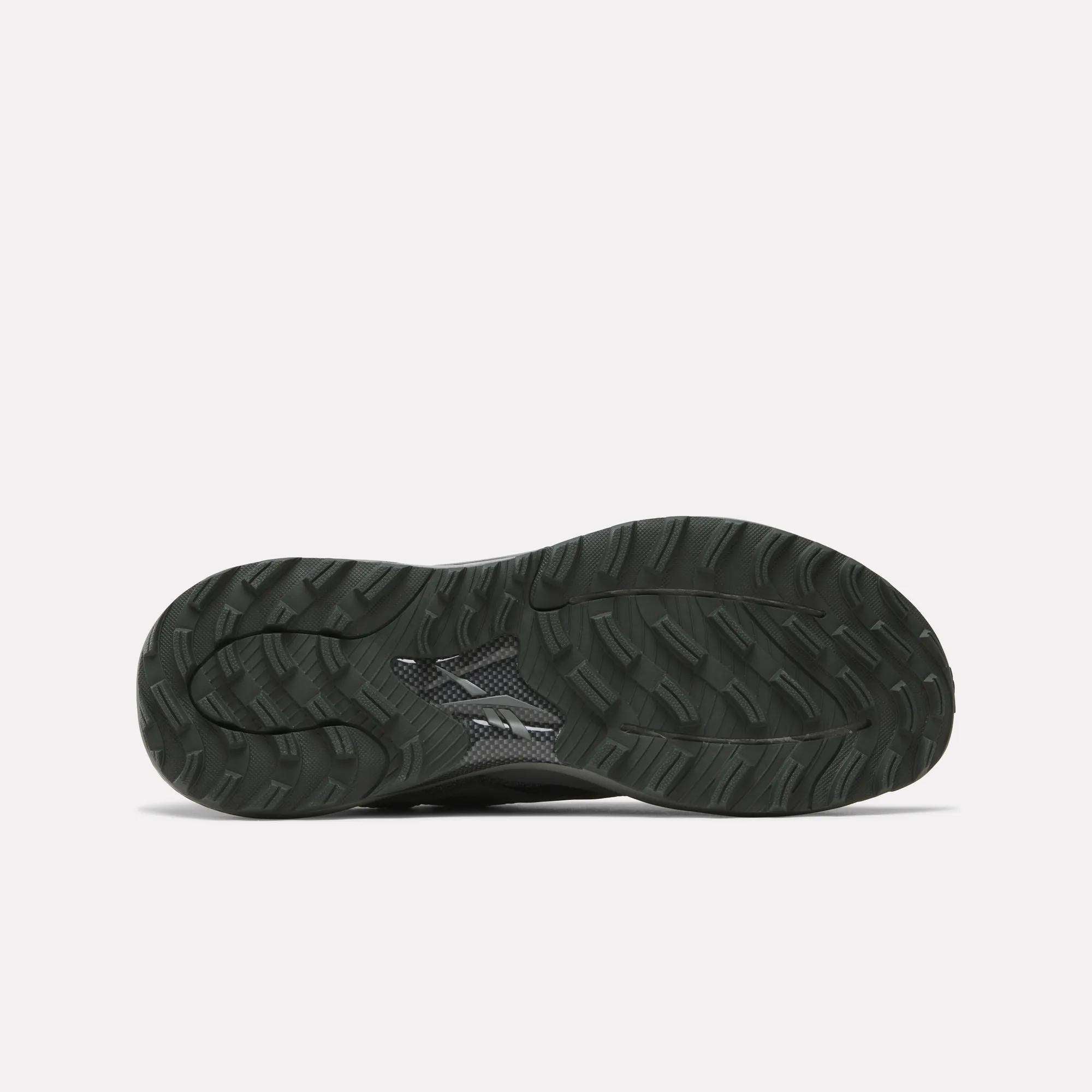 The image shows the black, textured rubber outsole of Reebok's Nano Golf Shoes with a wavy tread pattern and small logo near the center, designed to complement its lightweight FlexWeave upper. The background is plain white.