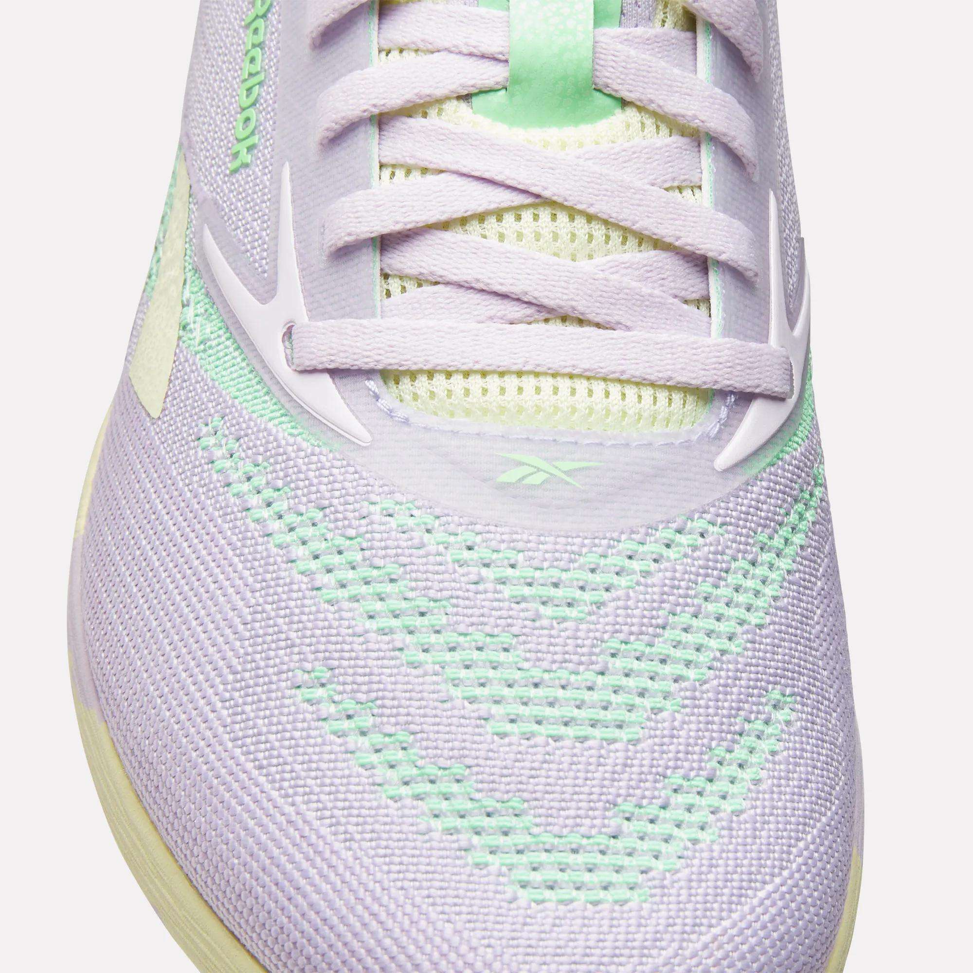 Close-up of Reebok Women's Nano X5 Training Shoes in pastel purple with mint green accents and white laces. Mesh material and detailed stitching on the toe and upper ensure comfort, ideal for running or training.
