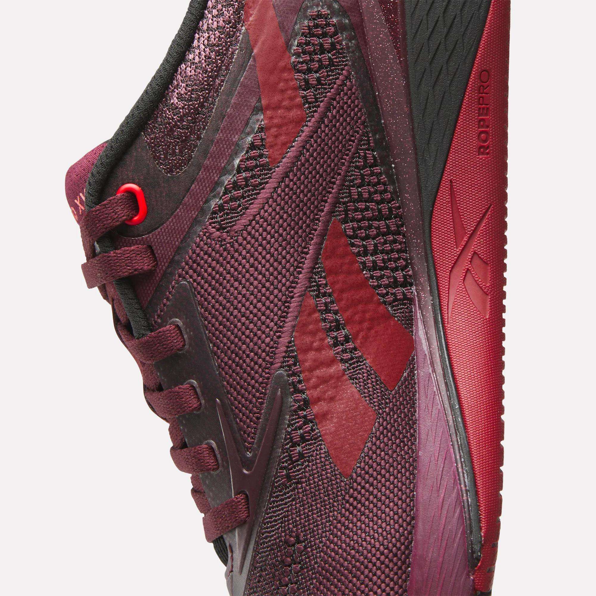 Close-up of Reebok Women's Nano X5 Training Shoes in maroon and black, featuring detailed mesh texture, laces, side logo, and a black-red sole with "ROPEPRO" near the heel—ideal for women’s shoe collections.