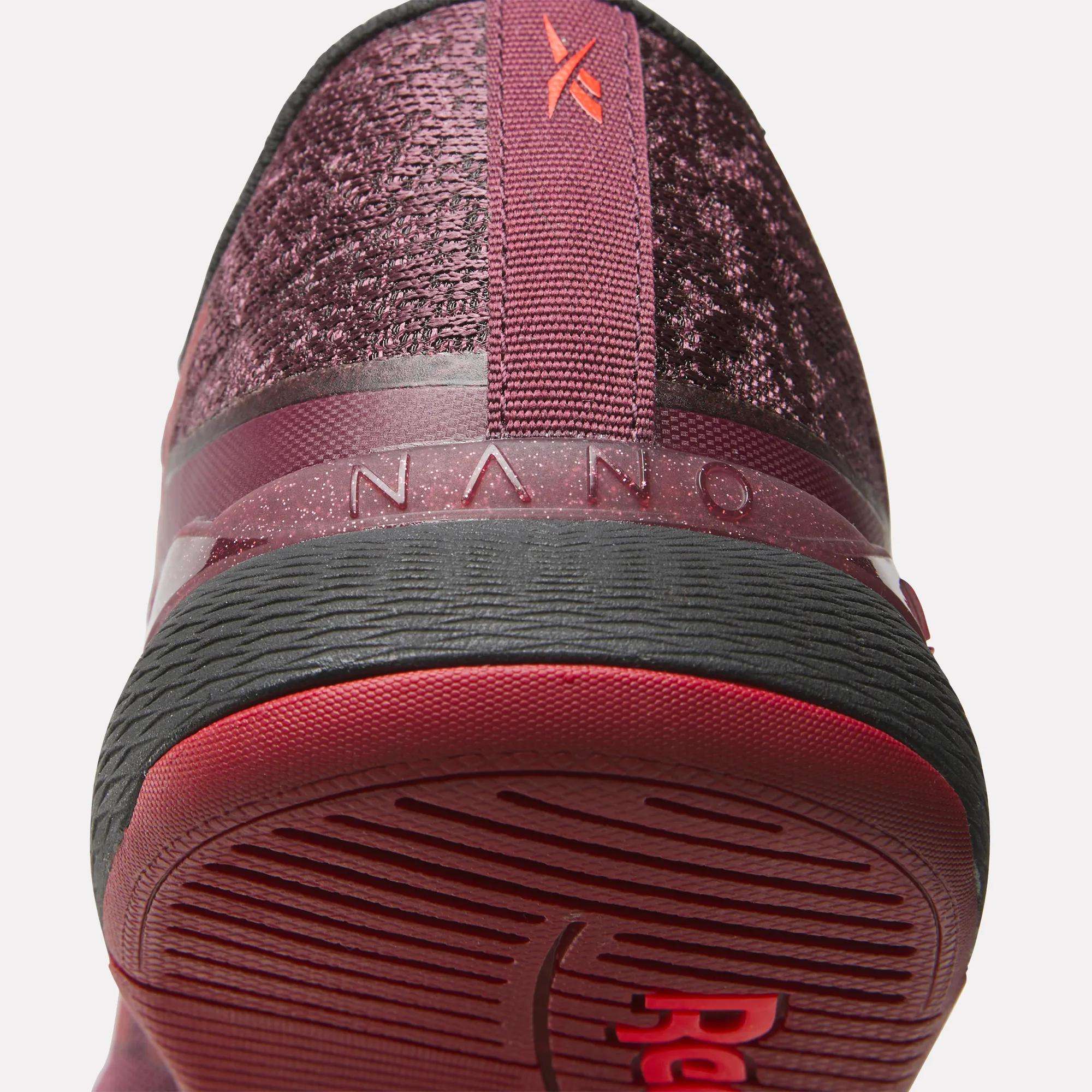 Close-up of the heel and sole of Reebok Women's Nano X5 Training Shoes in burgundy, featuring textured fabric, a red pull tab, "NANO" on the back, and a black and red rubber outsole for comfortable support.
