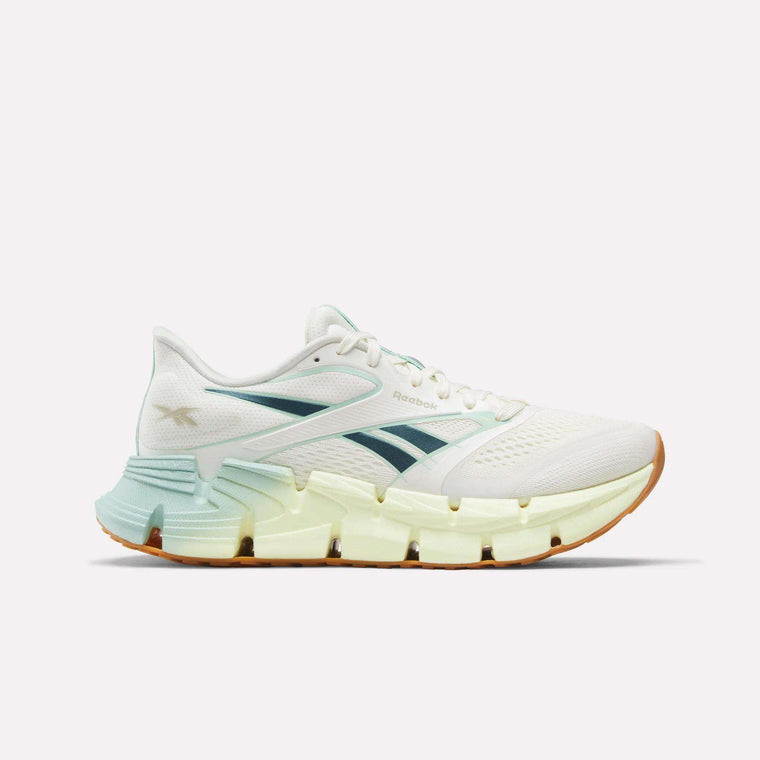 The Reebok Women's FloatZig 2 Running Shoes feature a white mesh upper for support, light green accents, a blue logo, and a chunky segmented sole with energy-returning cushioning in a gradient from pale yellow to gum brown.