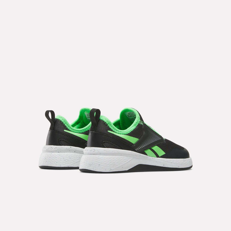 A pair of Reebok Nano Play Slip-On Shoes for little kids in black and neon green, featuring white soles, is shown from the back at a slight angle on a plain white background.