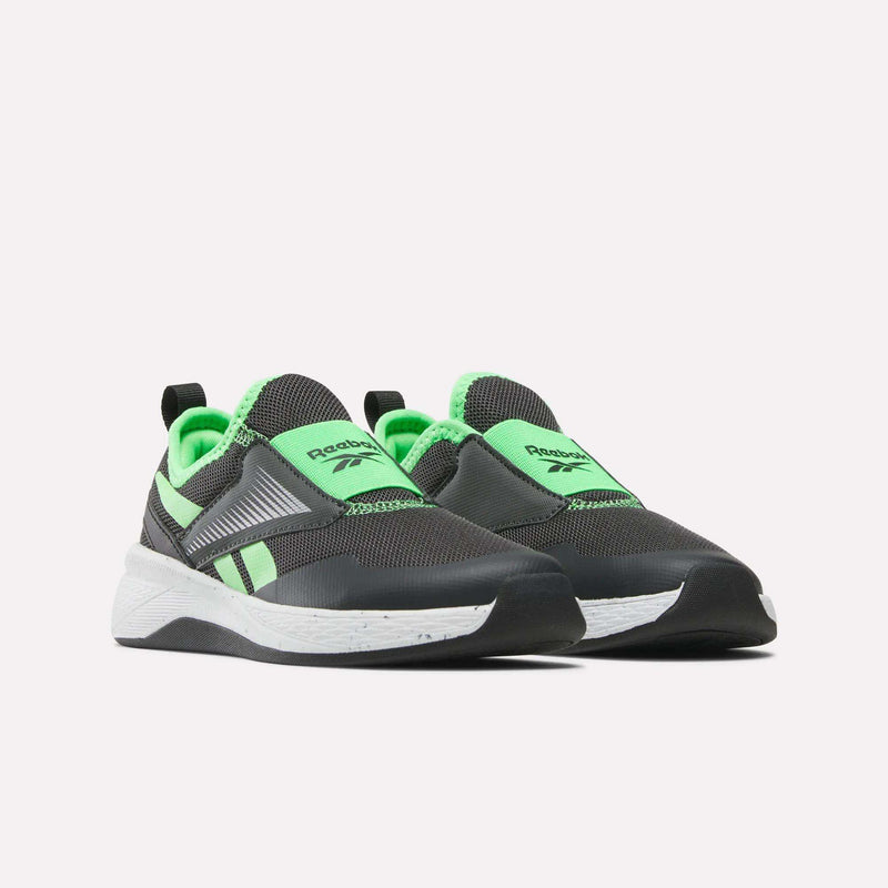 The Reebok Nano Play Slip-On Shoes for little kids feature a dark gray upper with bright green accents, white midsoles, and black outsoles. These trainers are shown against a plain white background.