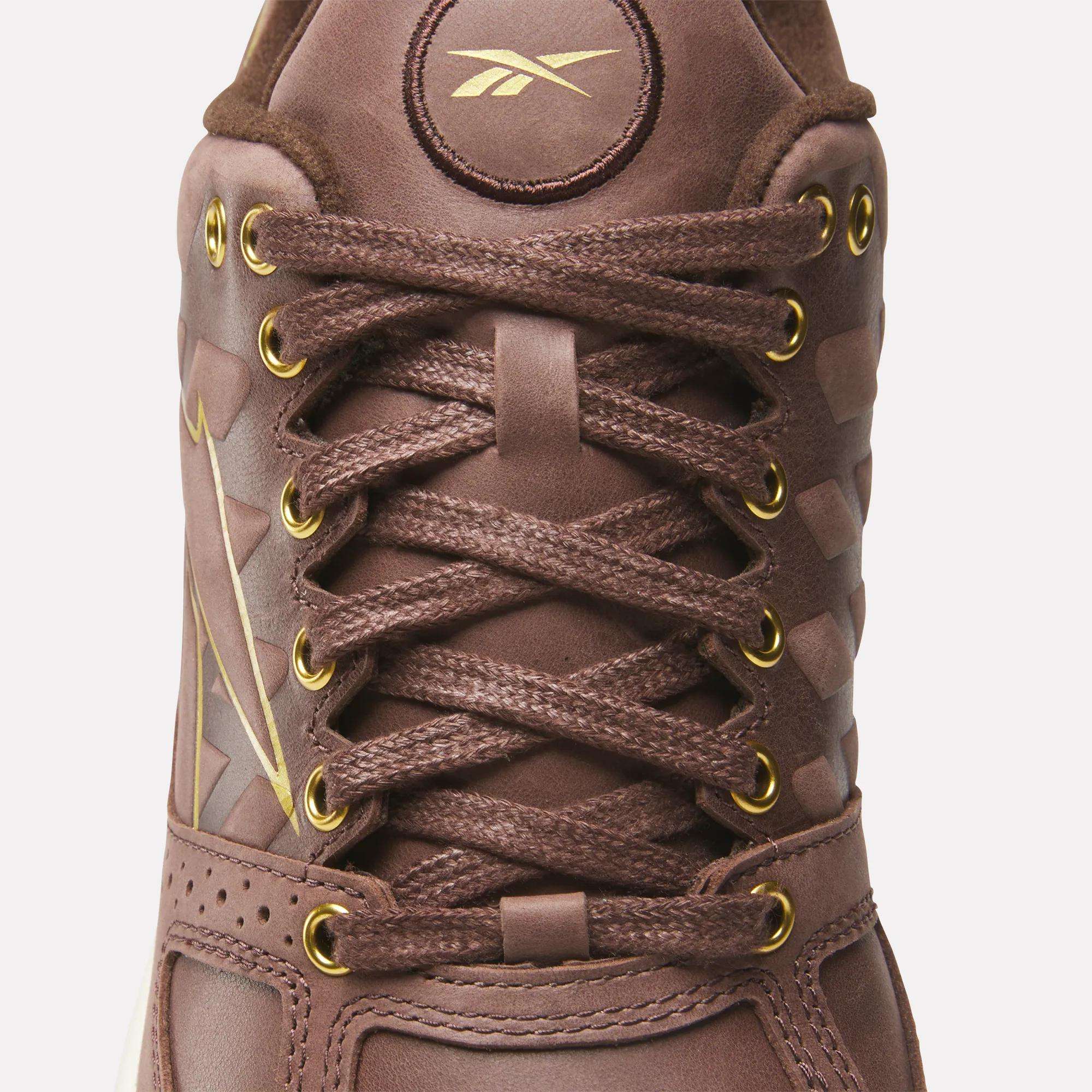 Close-up of Reebok Nano 2.0 Training Shoes in brown pebbled leather, with gold eyelets, brown laces, and gold Reebok branding on the tongue and side for a stylish, durable look.