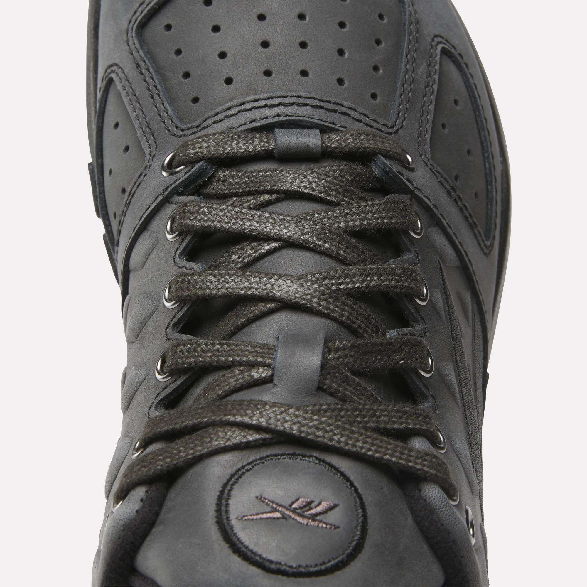 Close-up of the Reebok Nano 2.0 Training Shoes in black, featuring pebbled leather, laces, a perforated tongue, and stitched logo near the toe. Matte finish and detailed stitching around the laces enhance its premium look.