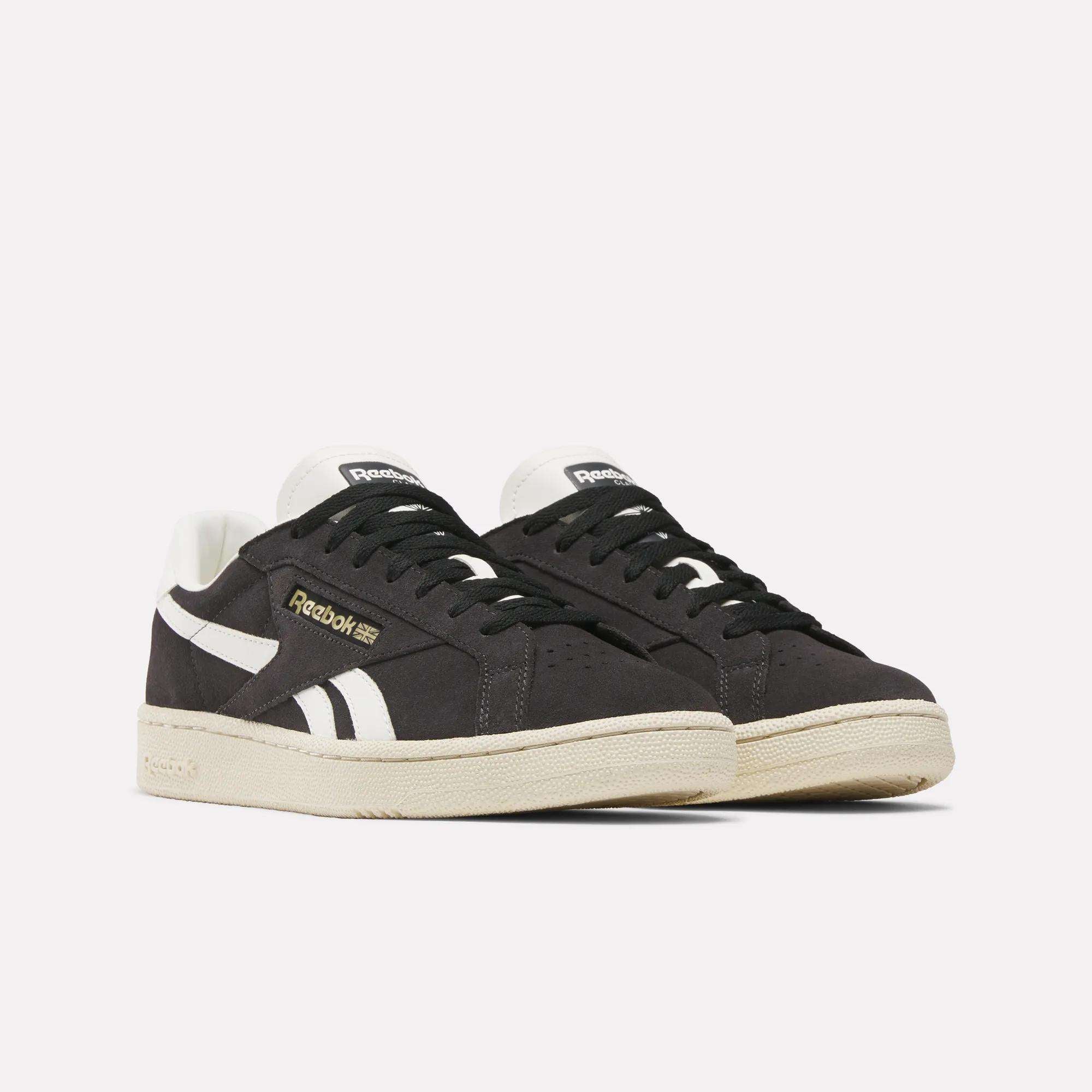 A pair of Reebok Club C Ground UK Shoes featuring a black suede upper, white accents, beige soles, and metallic gold side branding, showcased against a plain white background.