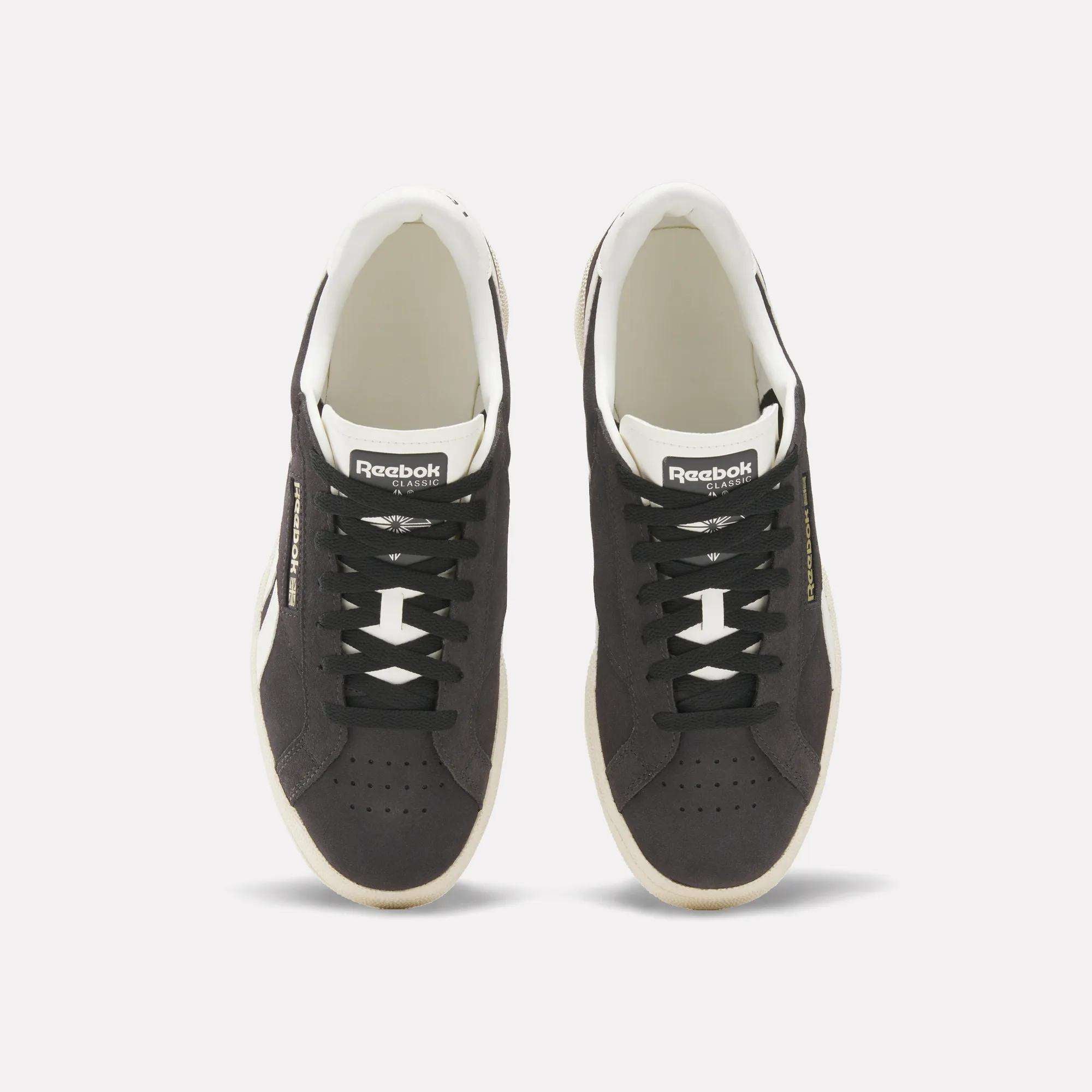 A pair of black Reebok Club C Ground UK Shoes with white soles and black laces, seen from above on a plain white background. The sneakers display metallic gold Reebok branding, with logos visible on the tongue and sides.