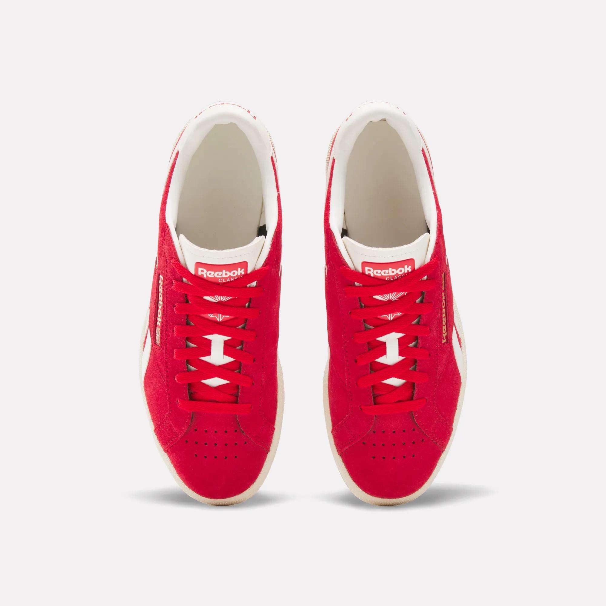 Top view of a pair of Reebok Club C Ground UK Shoes in red with white accents, white soles, suede upper, metallic gold branding, and matching red laces, displayed side by side on a plain white background.