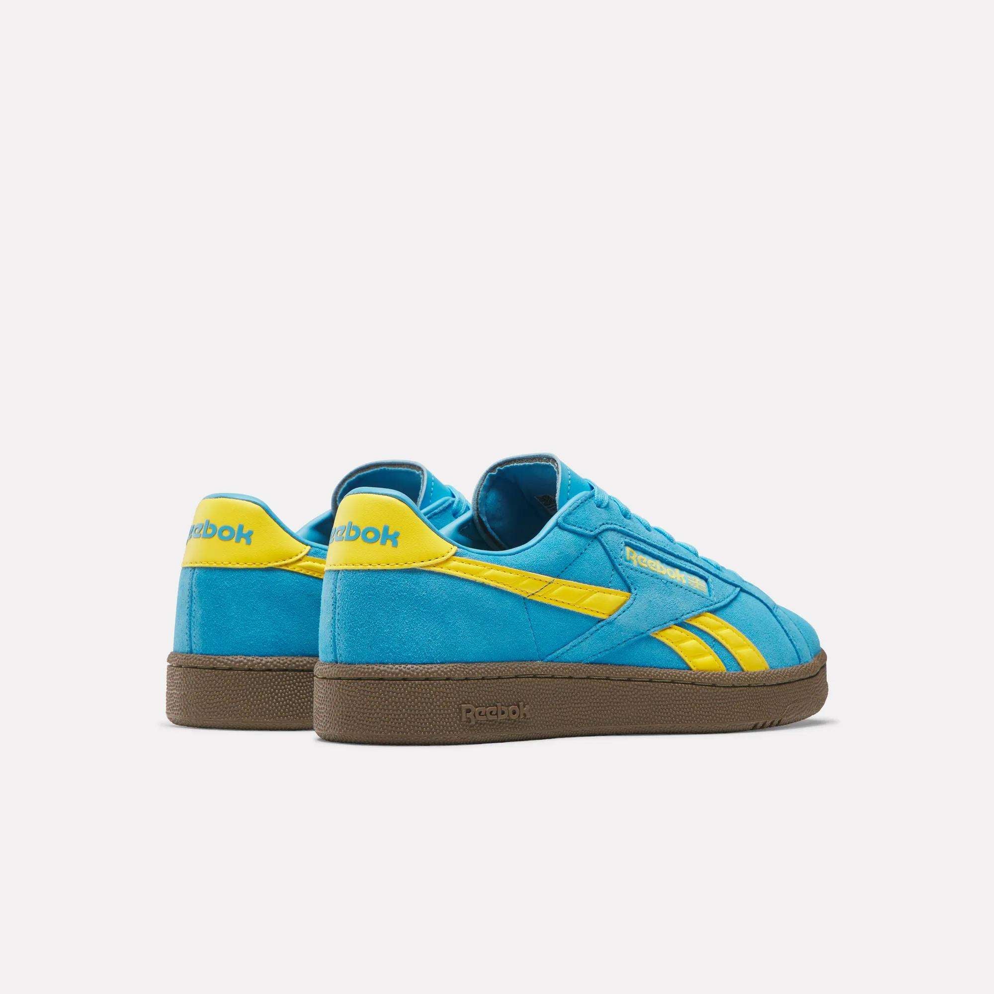 A pair of Reebok Club C Grounds UK Shoes with blue suede uppers, yellow accents, and brown soles is shown against a plain white background.
