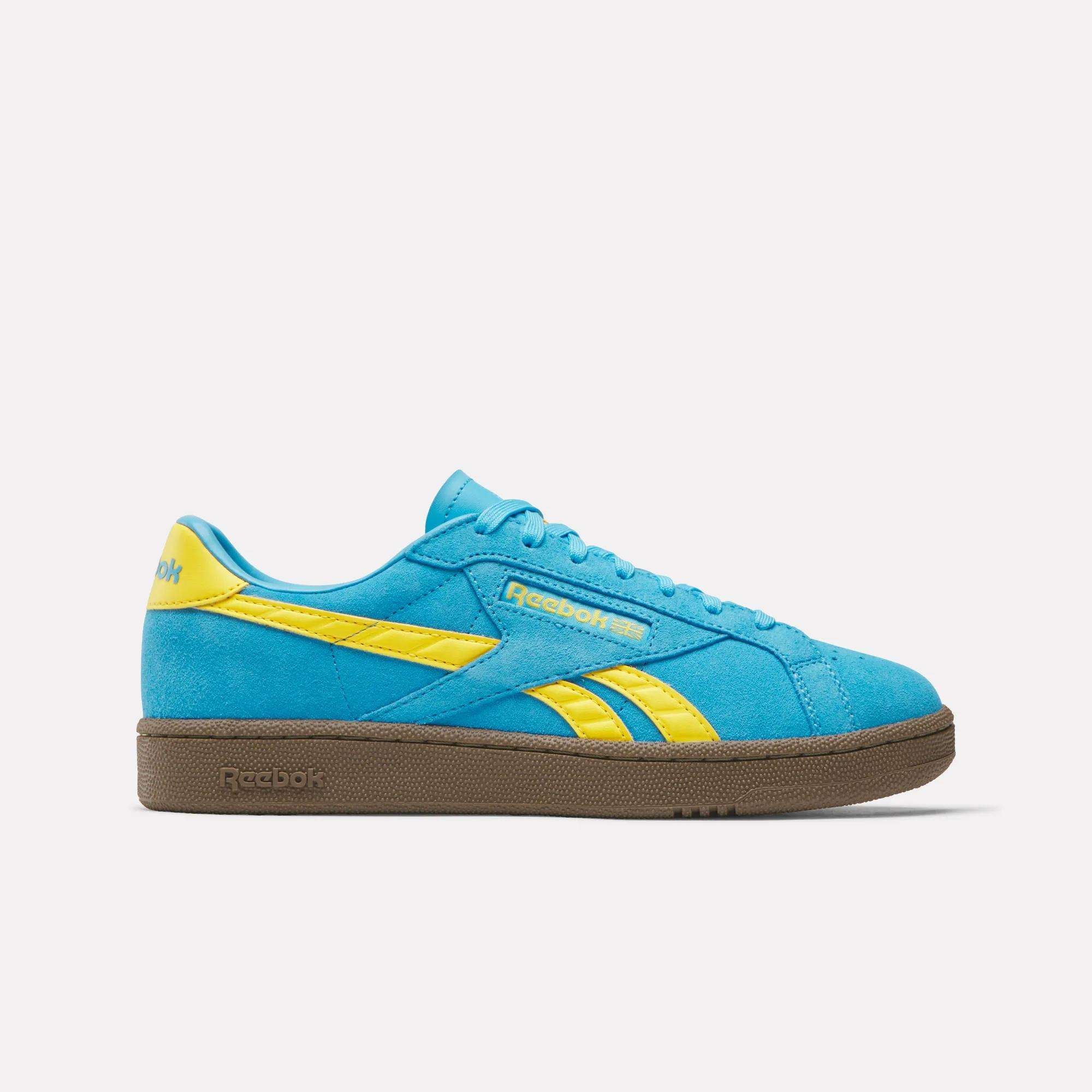 The Reebok Club C Grounds UK Shoes feature a blue suede upper with yellow accents and branding, brown rubber sole, and are pictured in side profile on a plain white background.